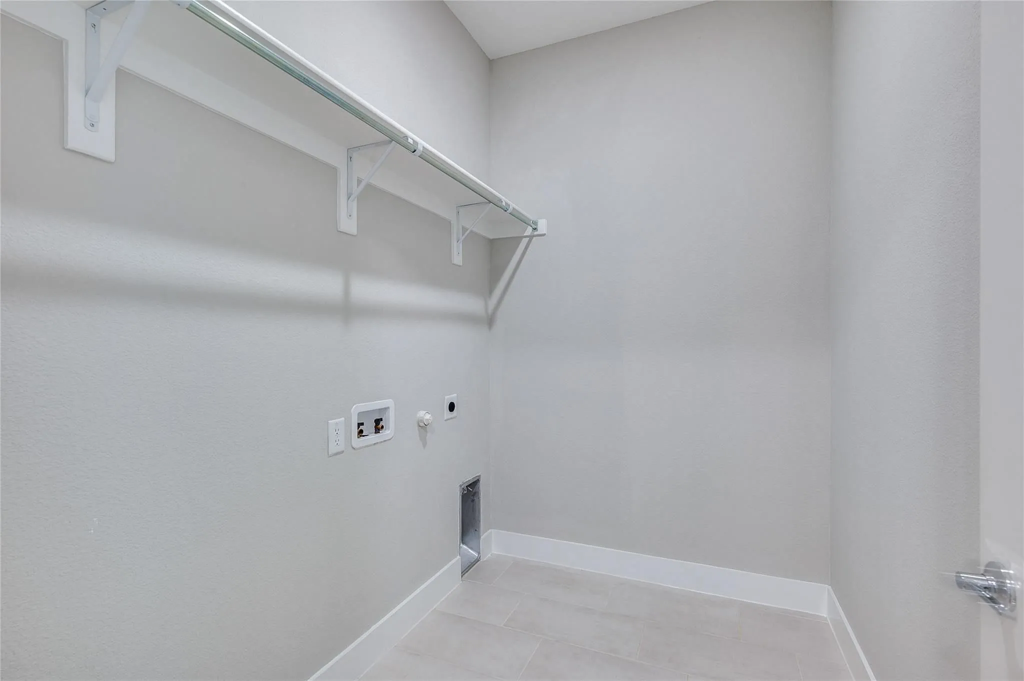 Laundry room with light gray walls, built-in shelving, a clothes rod, and tile flooring