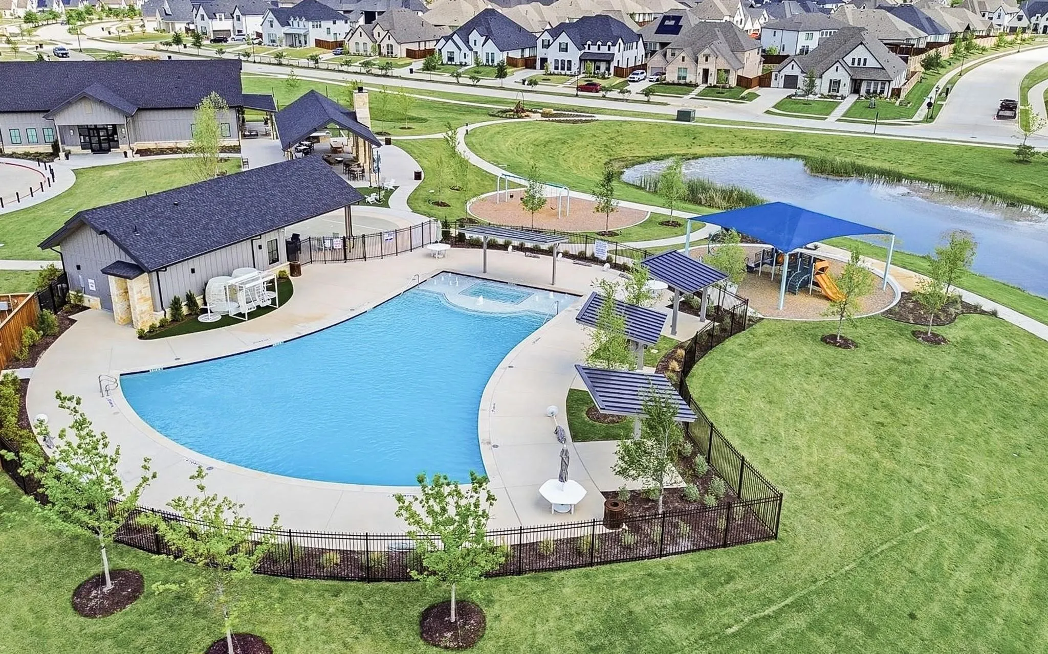 Expansive community pool with integrated spa and surrounding recreation areas, featuring a shaded playground, a covered open-air pavilion, and a separate community building