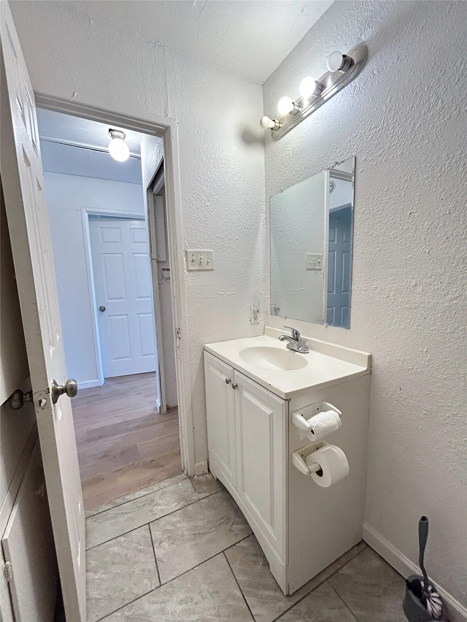 White vanity with integrated sink, chrome faucet, wall-mounted mirror, and tile flooring