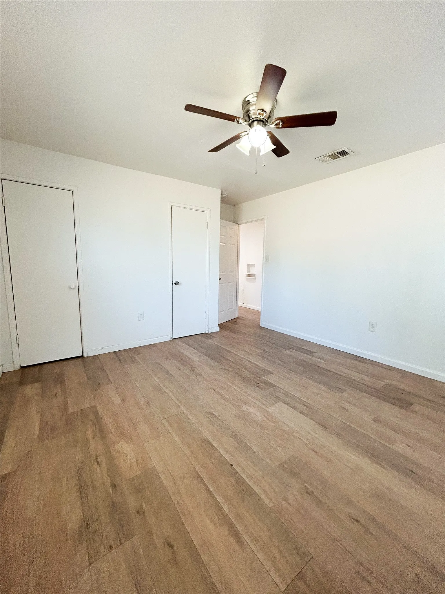 Wood-finish flooring, ceiling fan with integrated lighting, white walls, and white doors