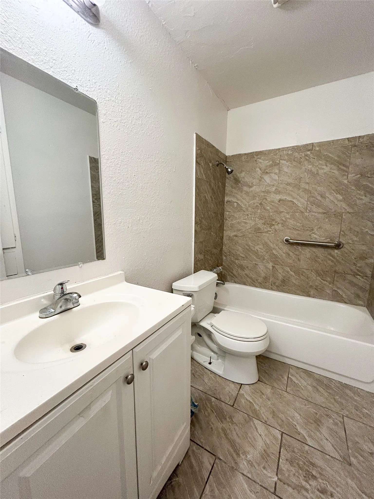 White vanity with an integrated sink, polished chrome faucet, full-width wall mirror, tile flooring, and a tiled shower/tub combination