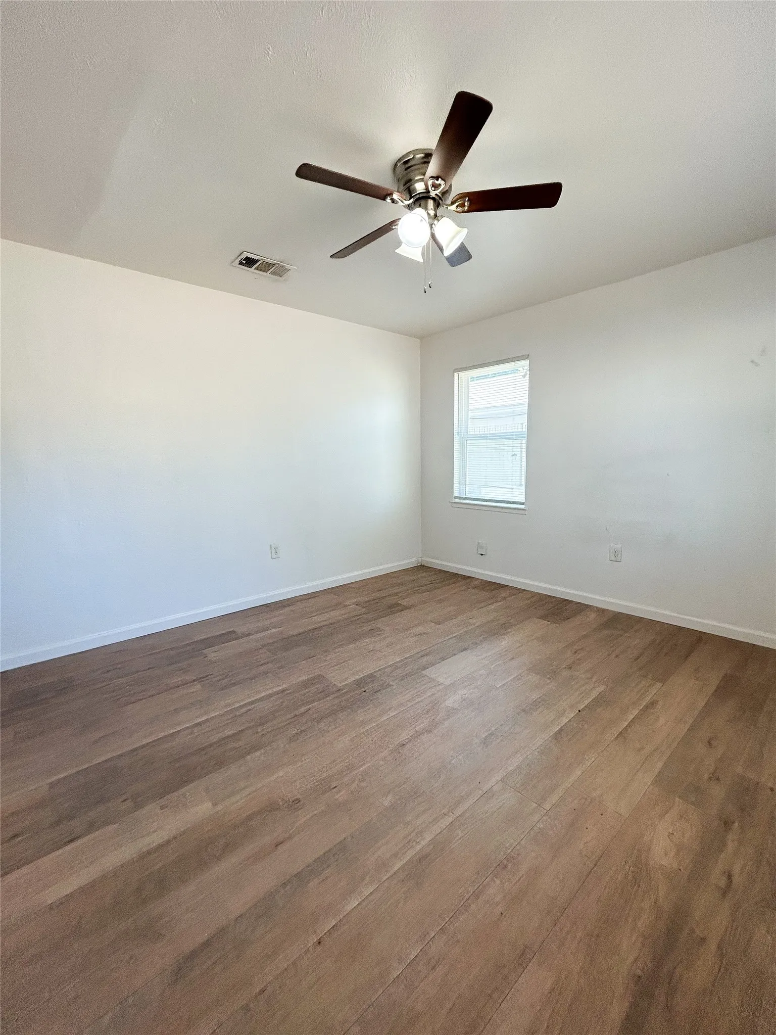 Wood-finish flooring, ceiling fan with integrated lighting, and a single window with blinds