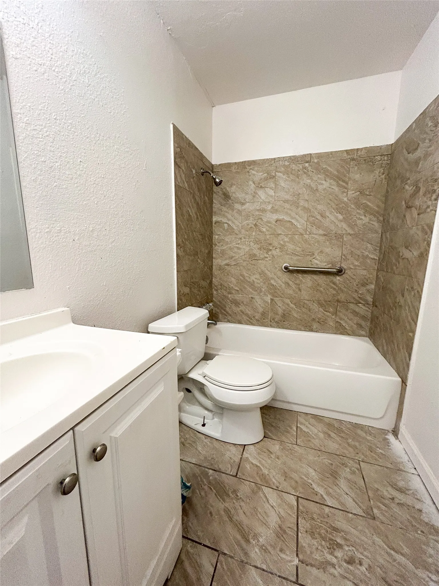 Ceramic tile flooring, white vanity with integrated sink, modern toilet, and a tiled shower/tub combination