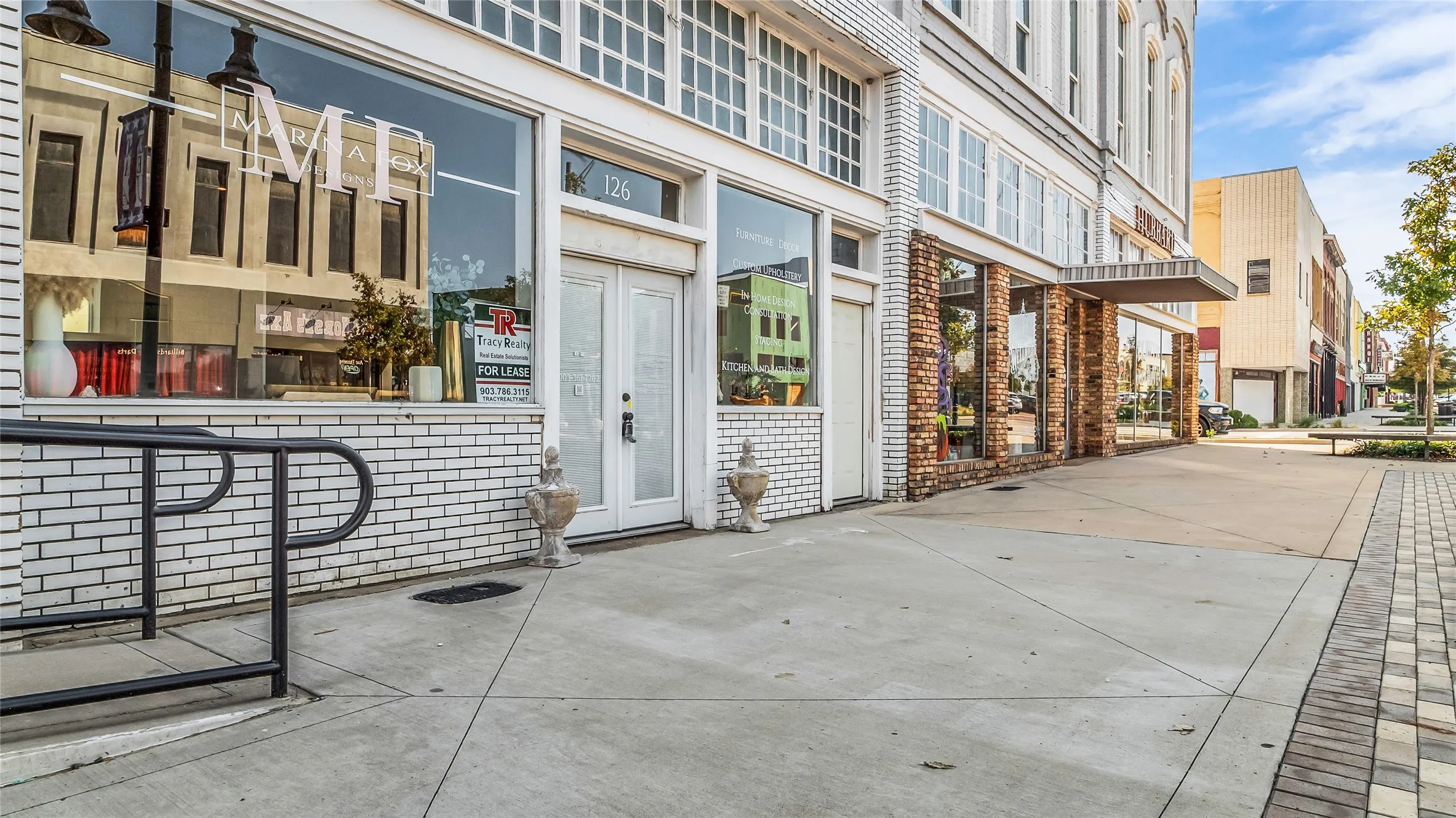 Brick facade with prominent storefront windows, double entry doors, building number 126, and concrete sidewalk