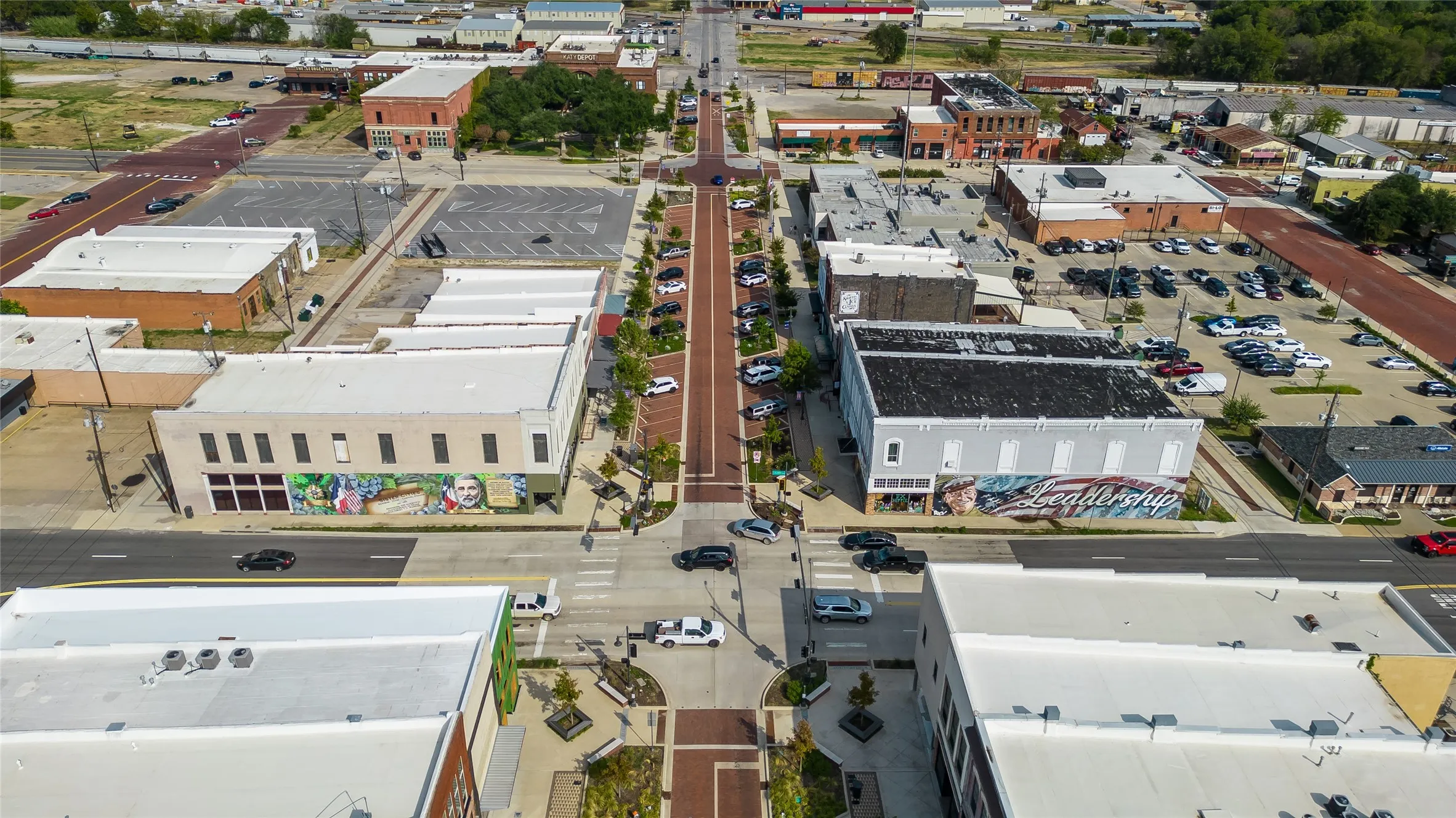 Aerial perspective of a commercial district featuring multiple buildings with diverse architectural styles, visible street parking, and established landscaping