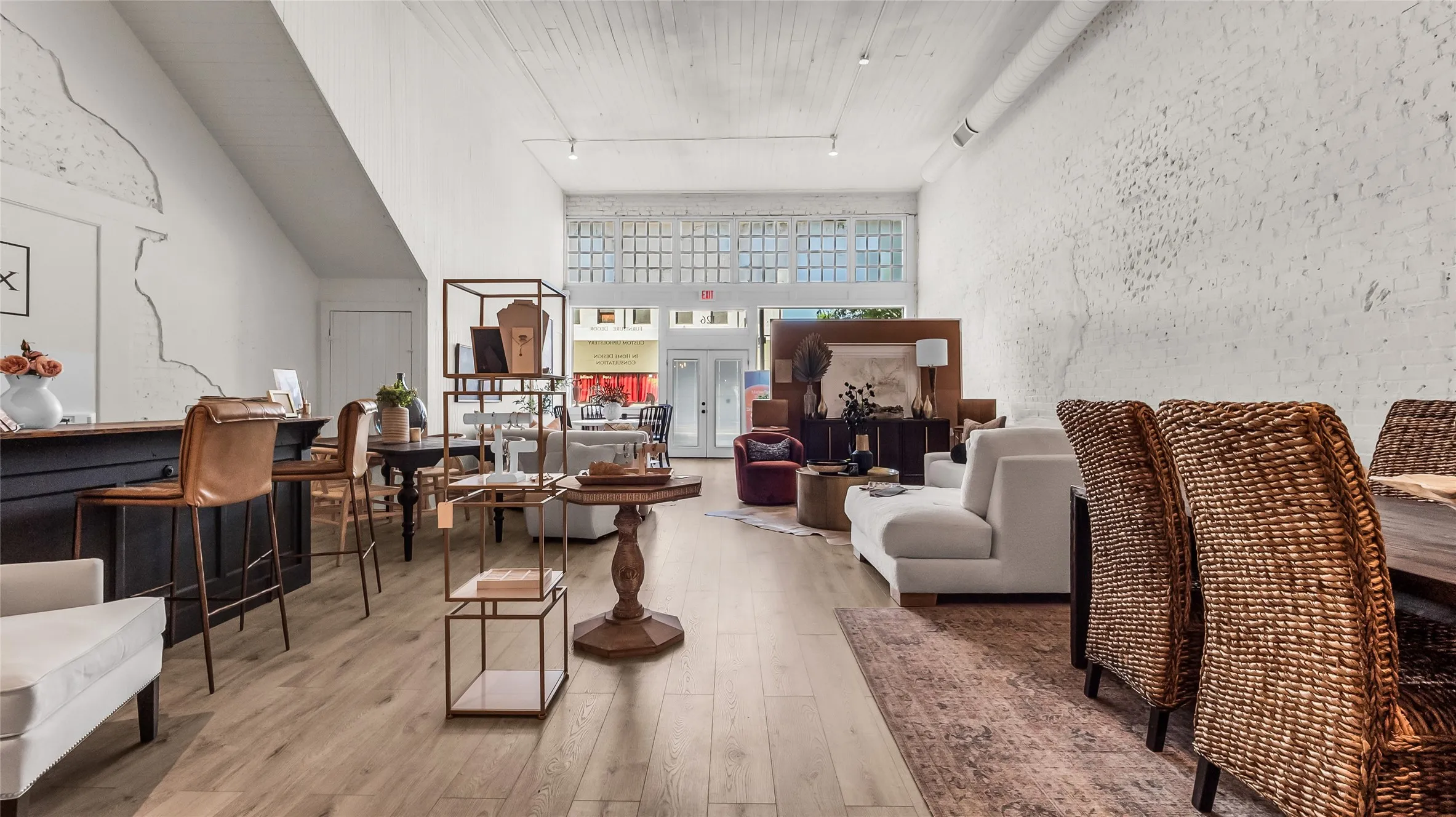 Tall ceilings, front-facing windows, wood-finish flooring, white brick walls, and track lighting