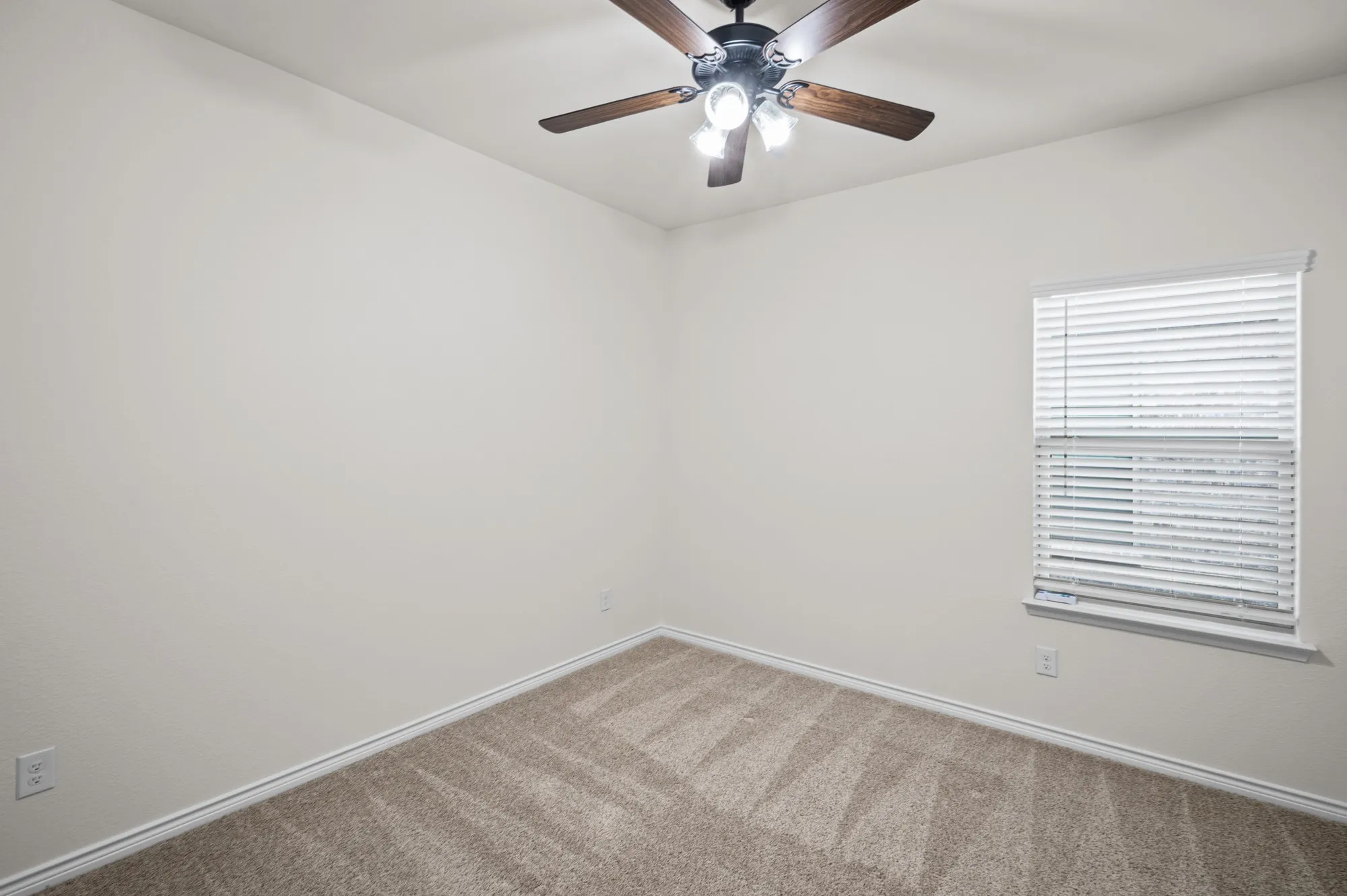 Neutral-toned carpeting, light-colored walls, window with horizontal blinds, and a ceiling fan with integrated lighting