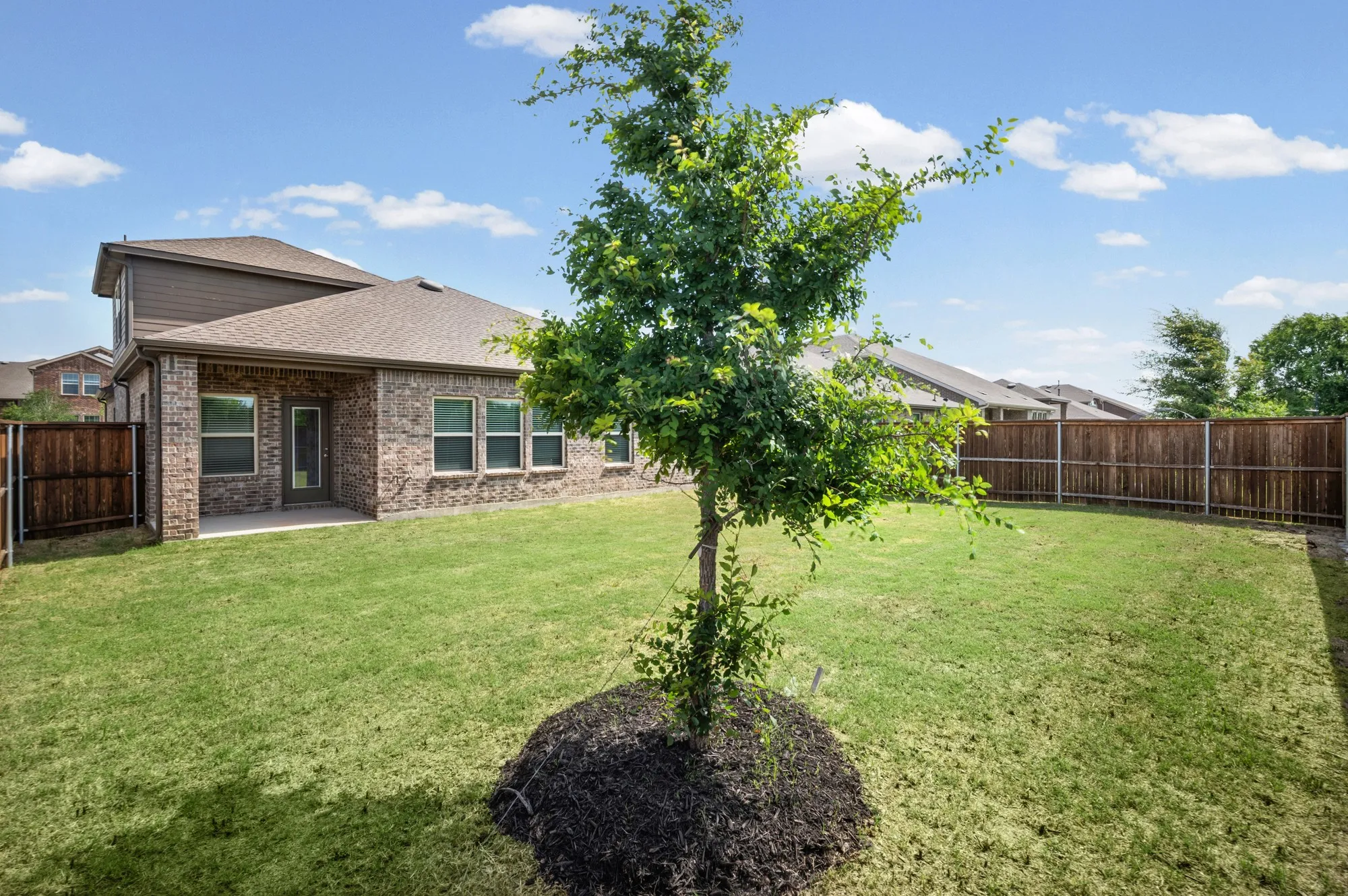 Expansive backyard featuring a manicured lawn, brick exterior, covered patio, and wood privacy fencing