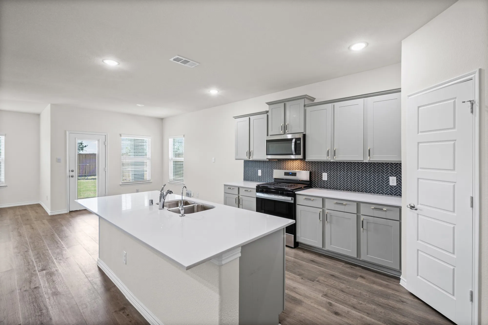 Kitchen featuring an island with dual basin sink, stainless steel appliances, grey cabinetry, and a patterned tile backsplash