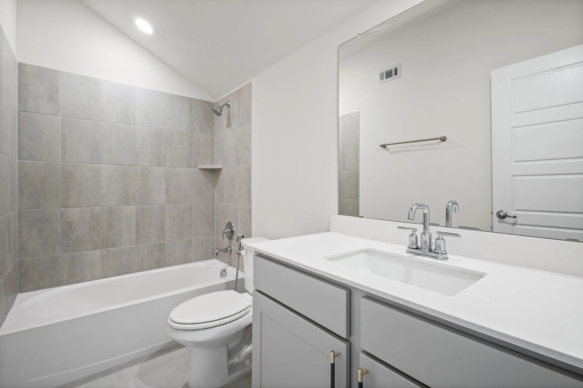 Integrated bathtub with subway tile surround, single vanity with light gray cabinetry, white countertop, and polished chrome fixtures