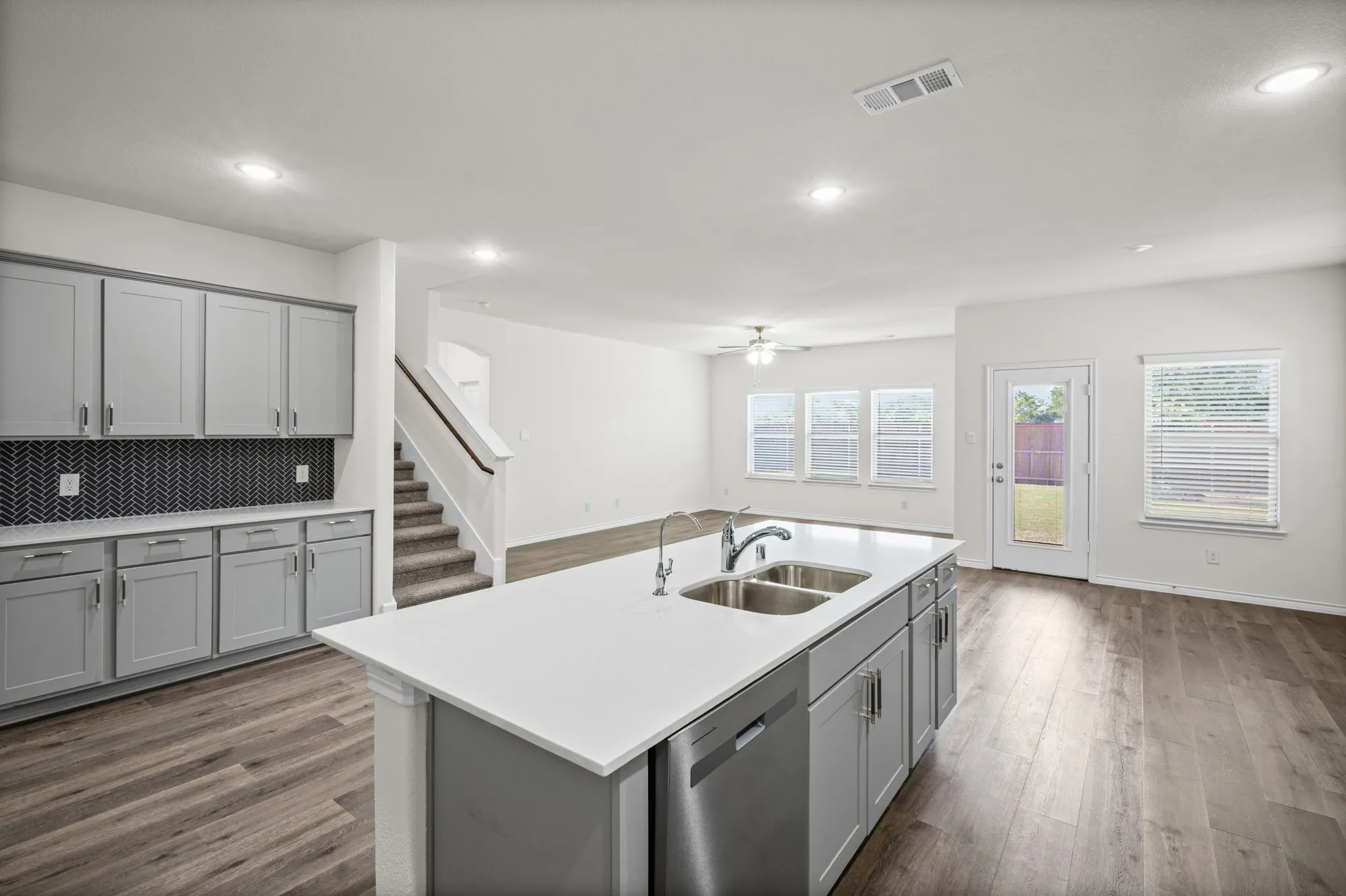 Kitchen featuring an island with double sinks, light gray cabinetry, dark herringbone-patterned backsplash, wood-finish flooring, and recessed lighting