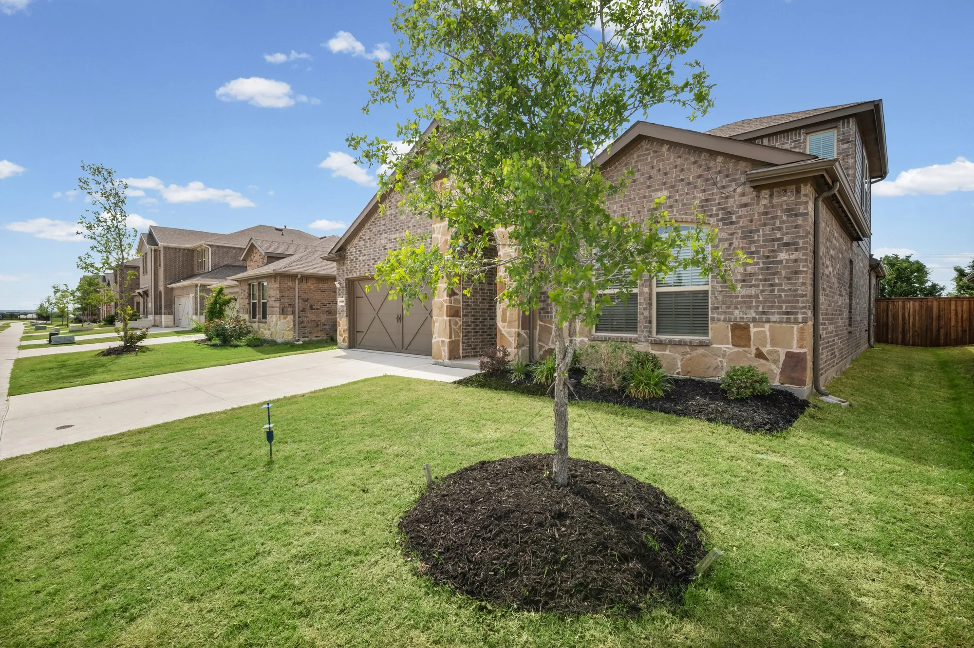 Brick and stone veneer exterior with a two-car garage, concrete driveway, and established landscaping