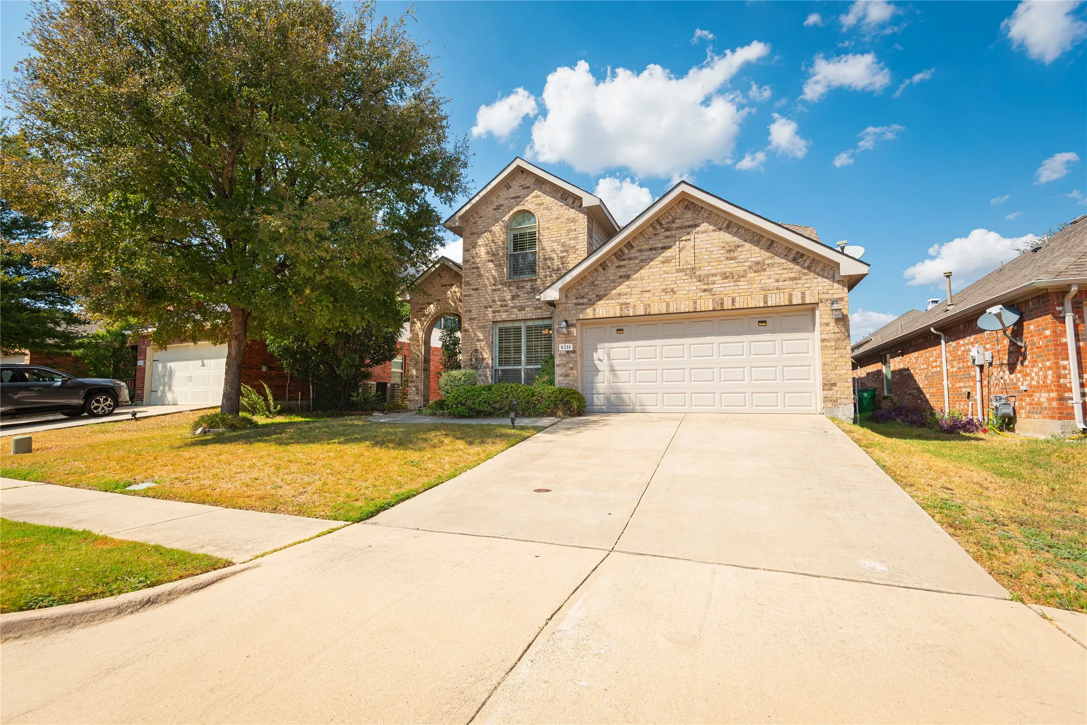 Brick exterior with an arched entry, attached garage, and established landscaping