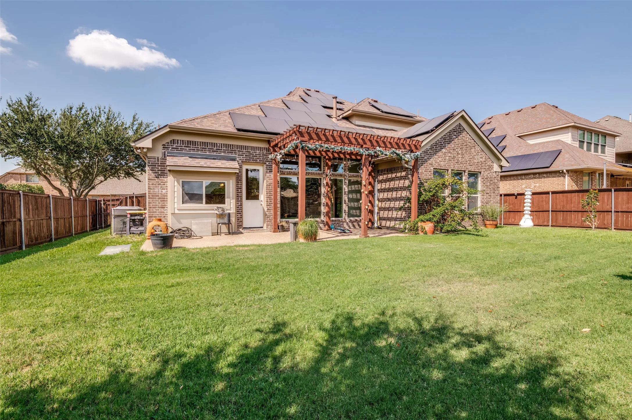 Expansive backyard showcasing a manicured lawn, mature landscaping, and a brick and stone exterior with a covered patio area featuring decorative brick detailing