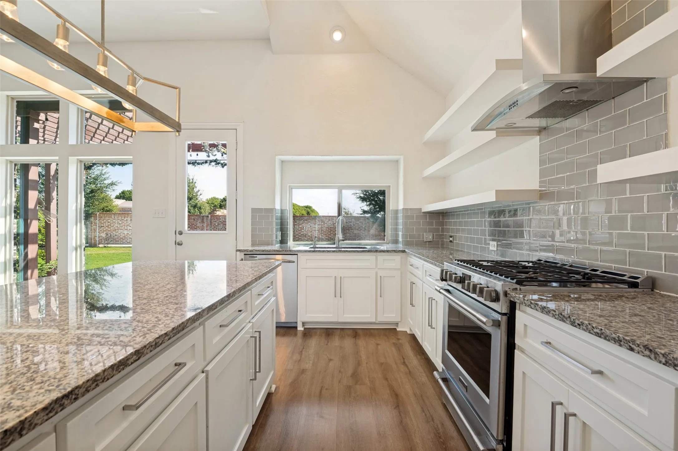 Vaulted ceiling, white shaker cabinetry, stainless steel appliances, granite countertops, and wood-finish flooring