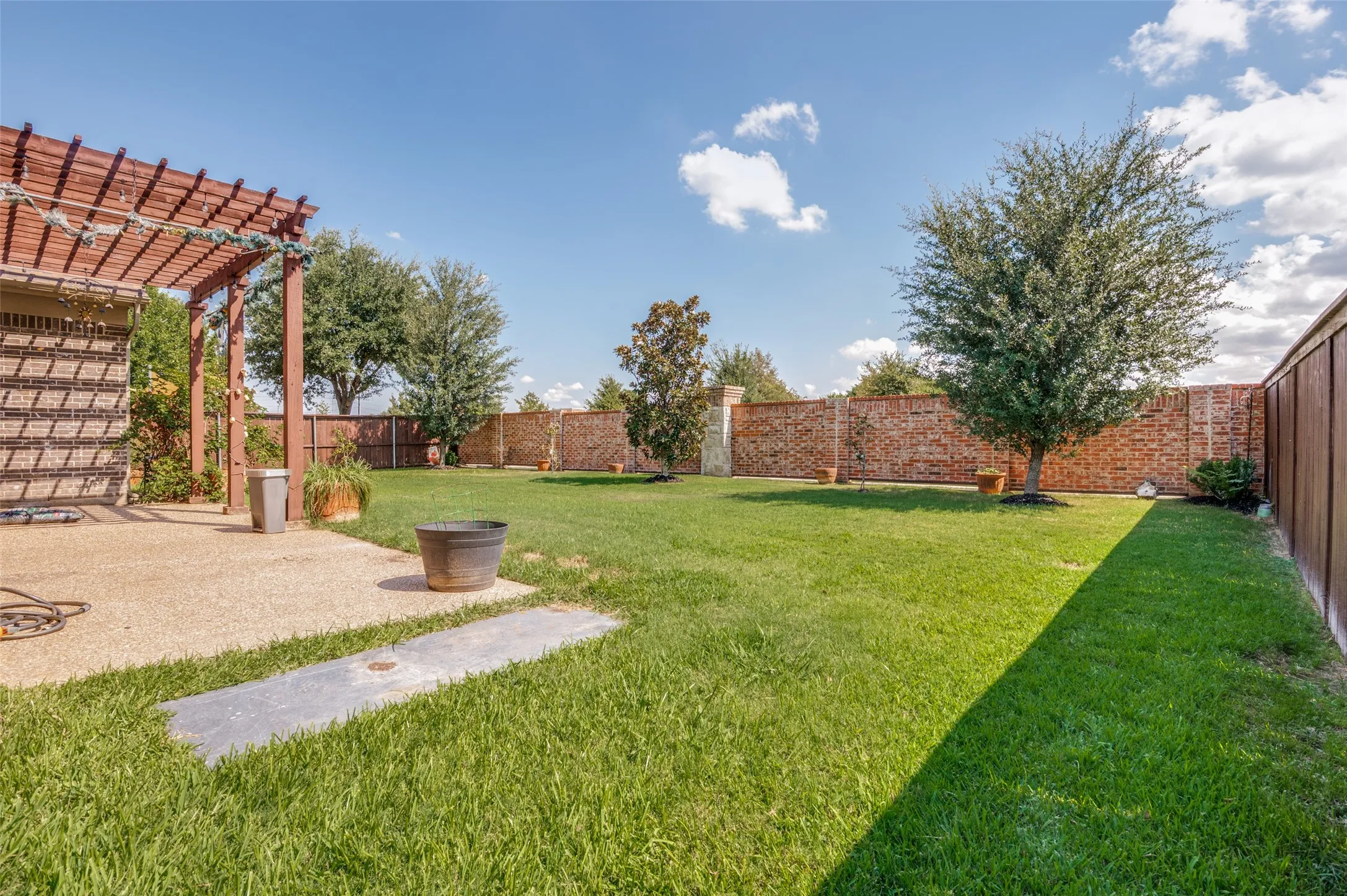 Expansive lawn featuring mature trees, a wood pergola, and a brick privacy fence