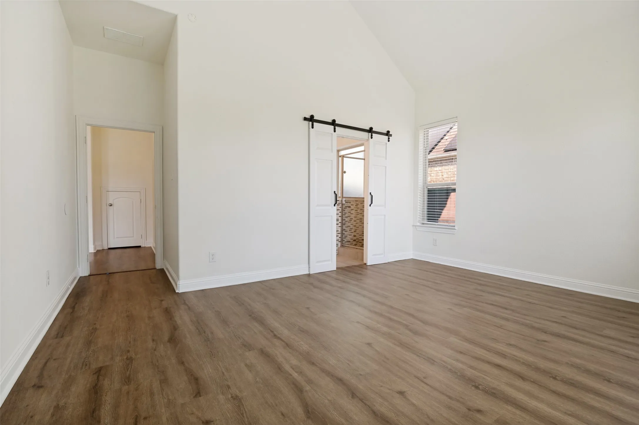 Vaulted ceiling, wood-finish flooring, white walls, window with blinds, and white barn doors