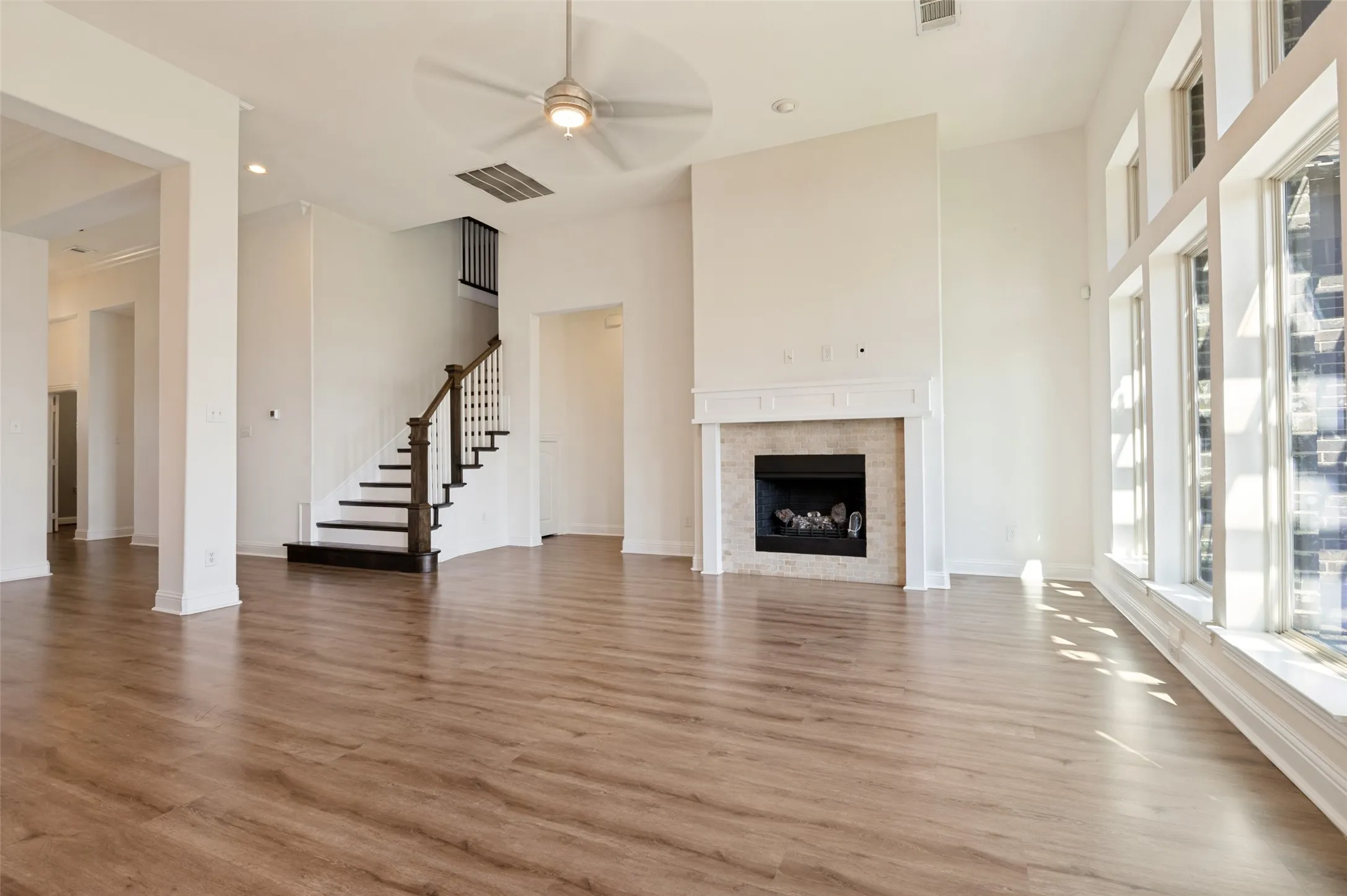 Wood-finish flooring throughout, a gas fireplace with a stone surround and mantle, and a staircase with dark wood treads and white risers