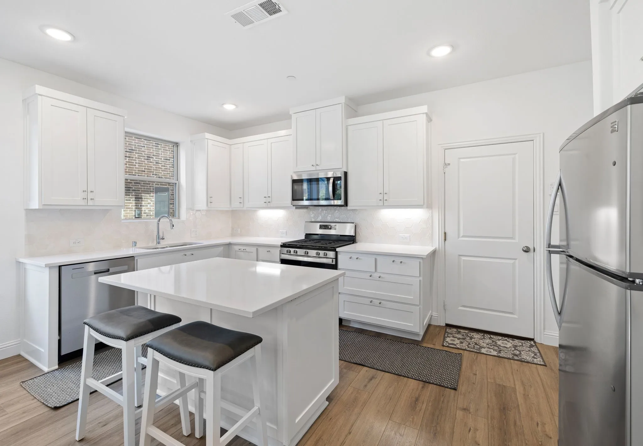 White shaker cabinetry, stainless steel appliances, wood-finish flooring, recessed lighting, and a kitchen island with a light-toned countertop