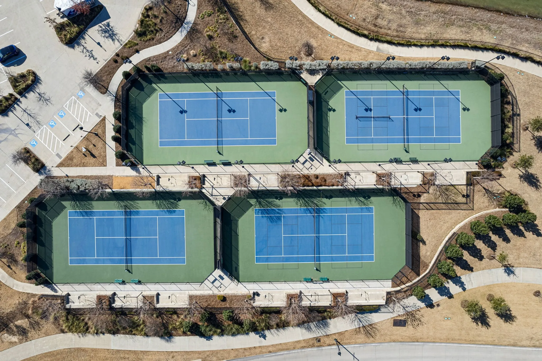 Four tennis courts with blue and green surfacing, surrounded by fencing