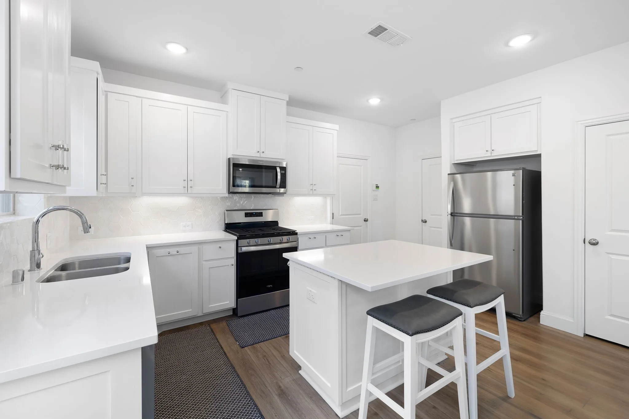 White cabinetry, stainless steel appliances, central island, dual basin sink, and wood-finish flooring