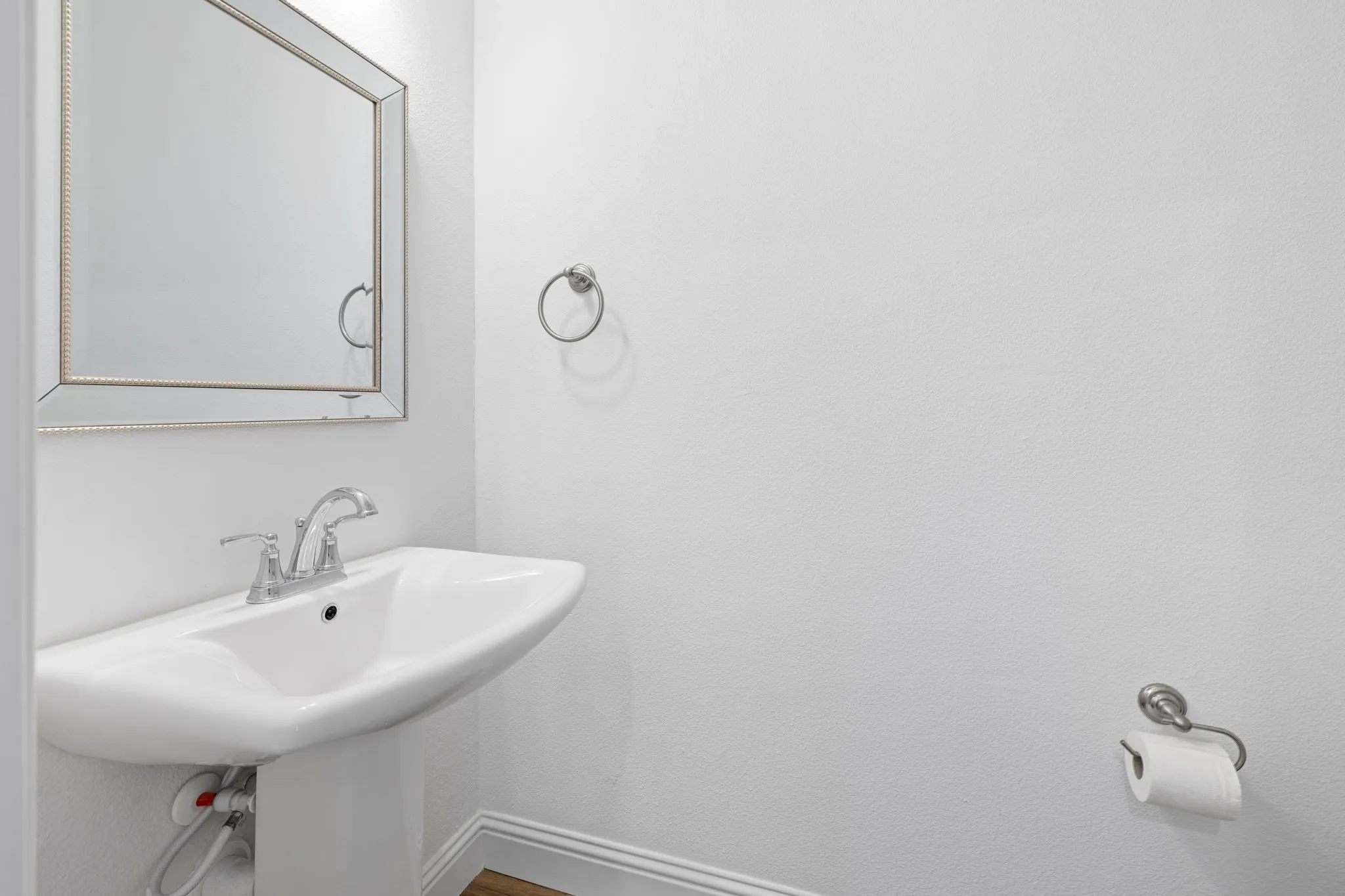 Pedestal sink with chrome fixtures, framed mirror, and towel ring