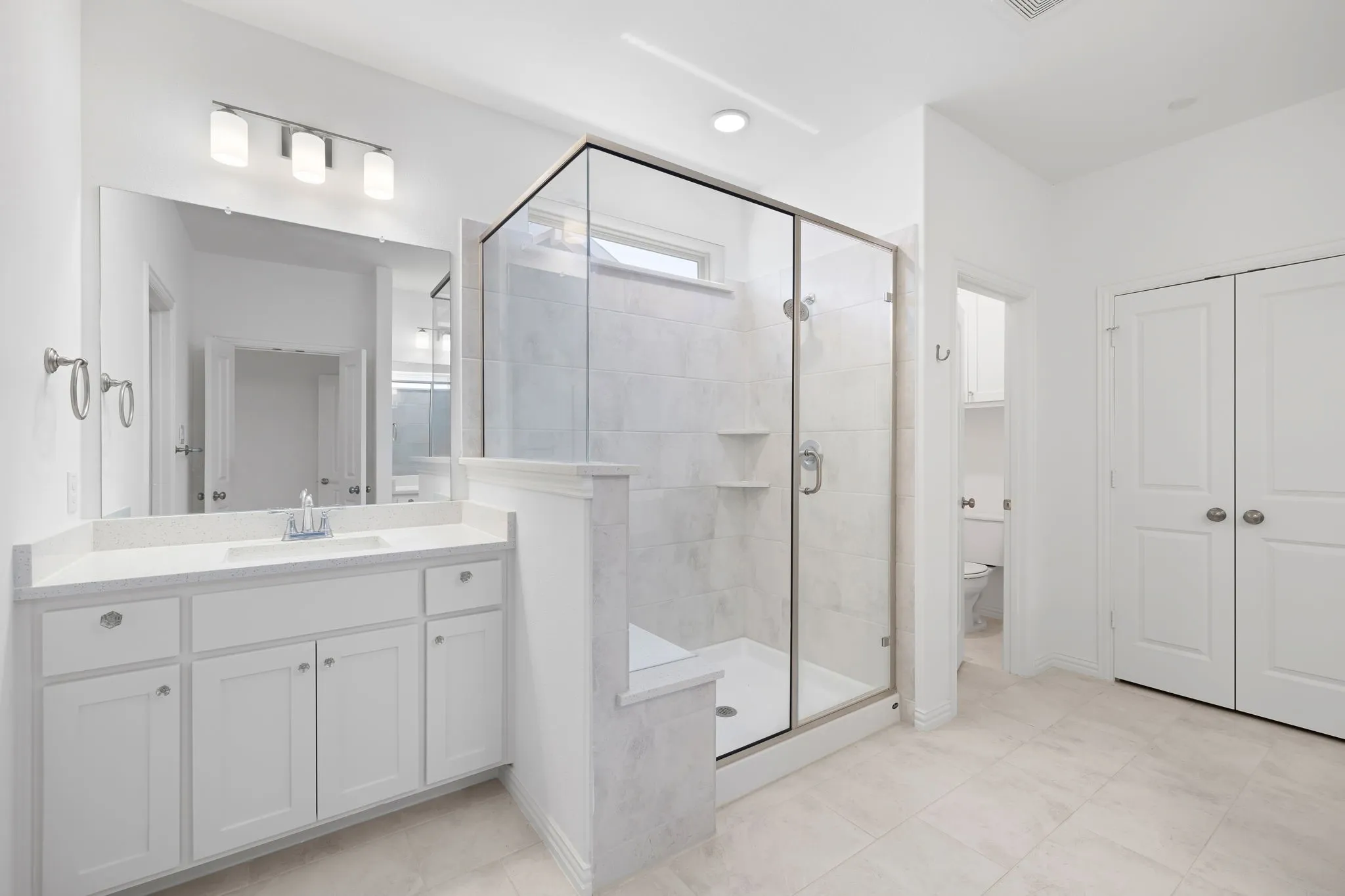White vanity with single integrated sink, framed glass shower enclosure, built-in shower bench, recessed shower shelving, and tile flooring