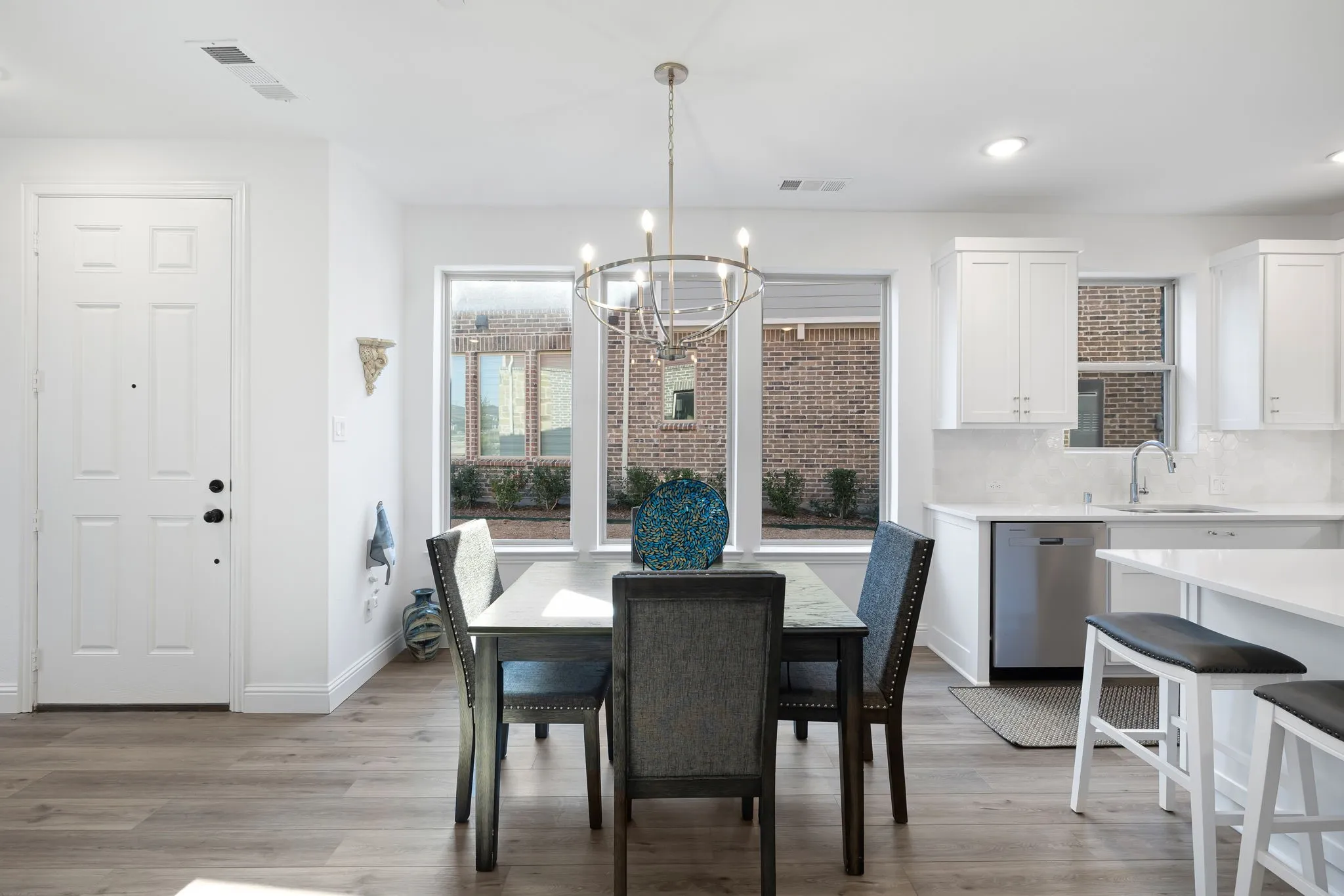 Wood-finish flooring, white paneled entry door, modern chandelier, white cabinetry, and stainless steel dishwasher