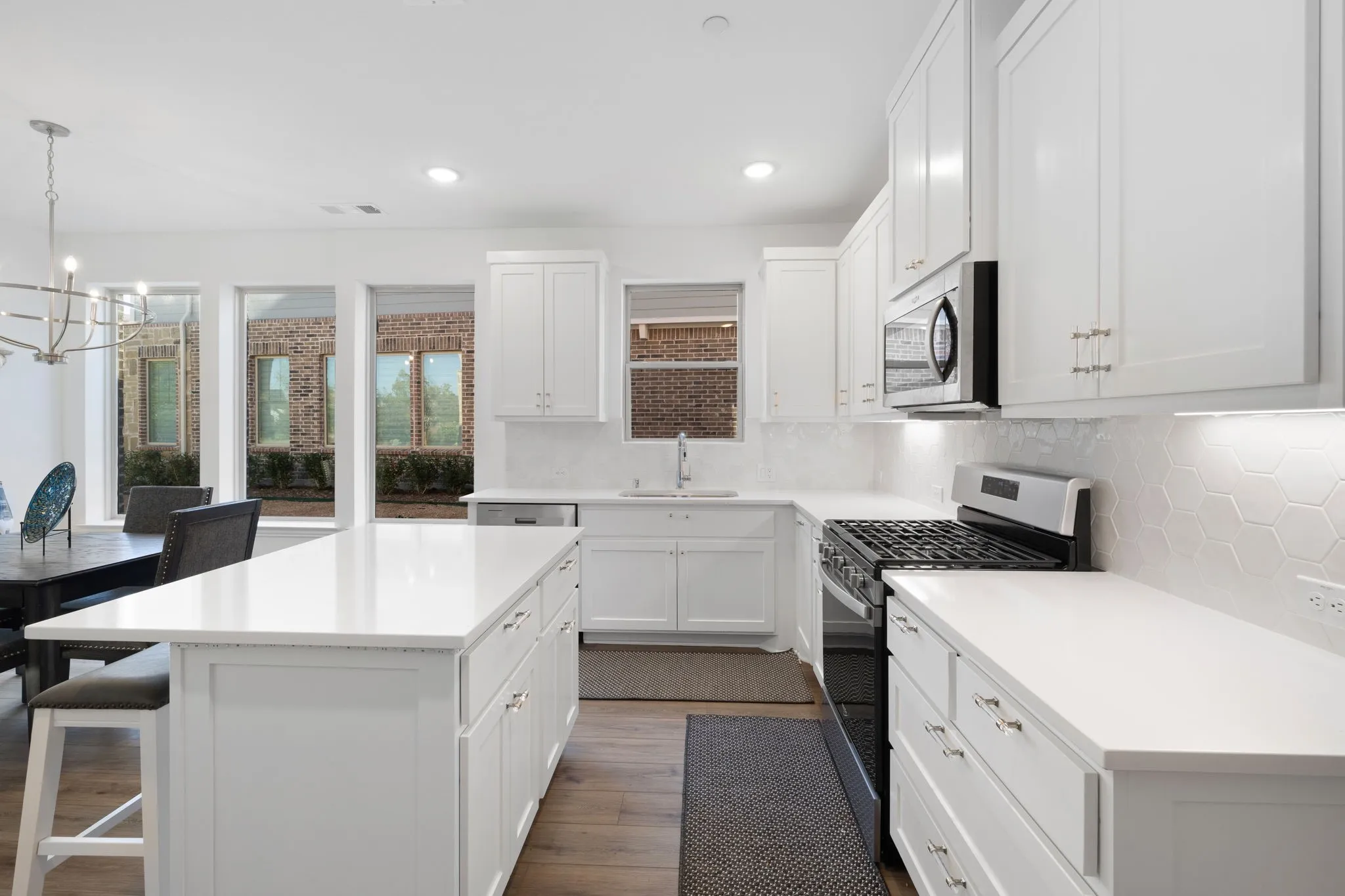 Chef's kitchen featuring white cabinetry with brushed nickel hardware, quartz countertops, a large center island with seating, stainless steel gas range, built-in microwave, and abundant natural light from French doors and transom windows overlooking the grounds