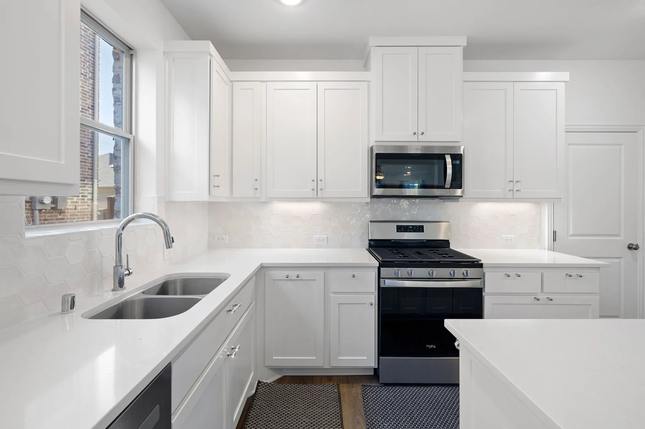 White shaker cabinetry with under-cabinet lighting, stainless steel appliances, solid surface countertops, a double basin undermount sink, and a geometric tile backsplash
