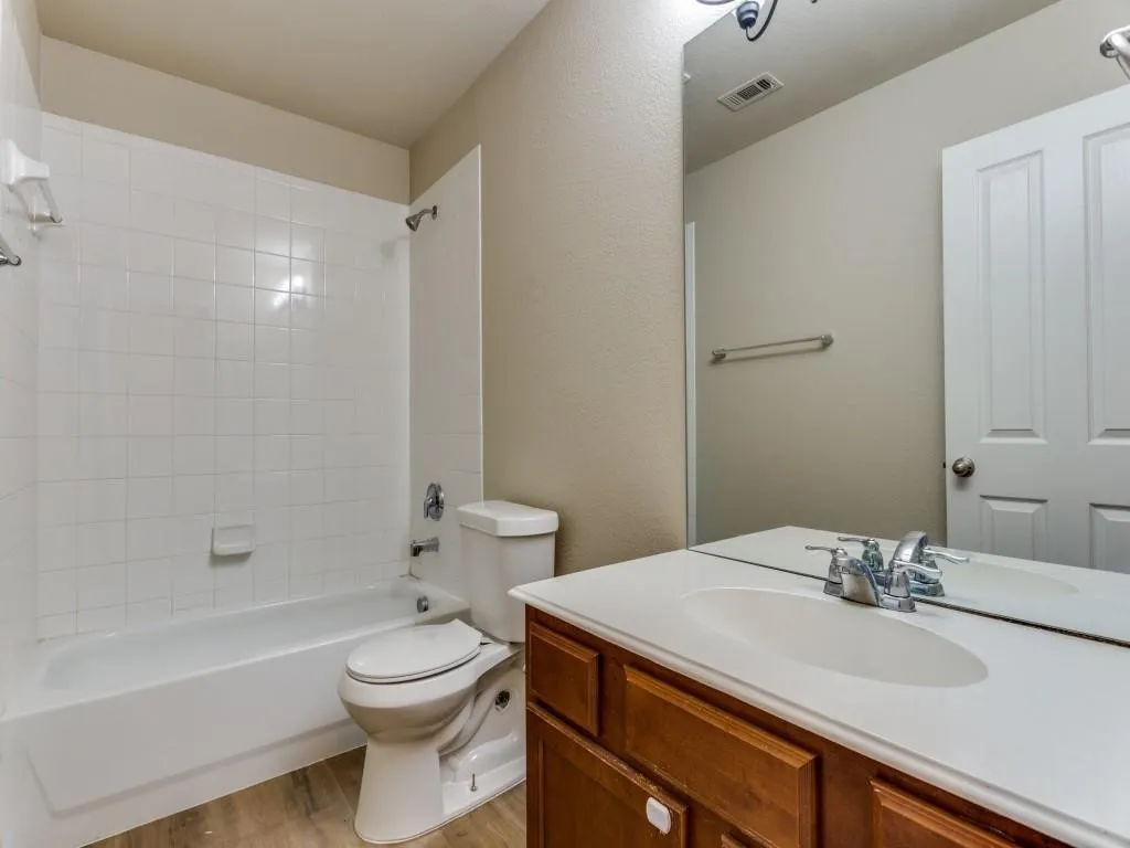 Bathroom featuring a white tile shower surround, integrated bathtub, wood-finish vanity with an integrated sink, and wood-finish flooring