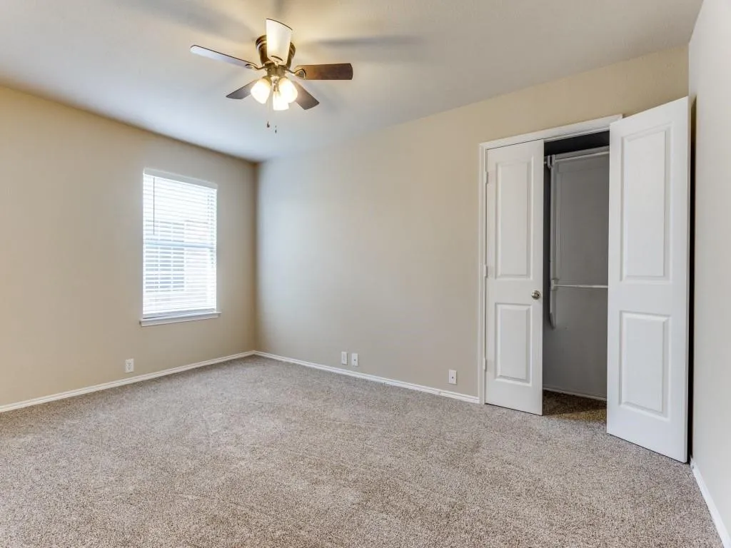 Neutral tone wall paint, carpet flooring, a window with blinds, a ceiling fan with integrated lighting, and a closet with bi-fold doors