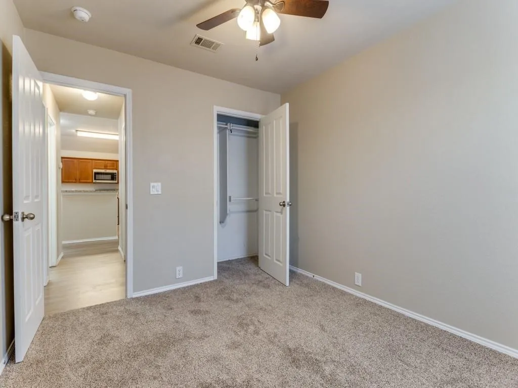 Plush carpeting, neutral wall tones, and a ceiling fan with integrated lighting