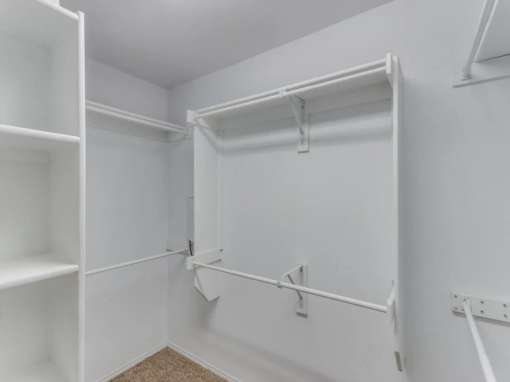 Closet featuring built-in shelving, multiple hanging rods, and neutral carpet flooring