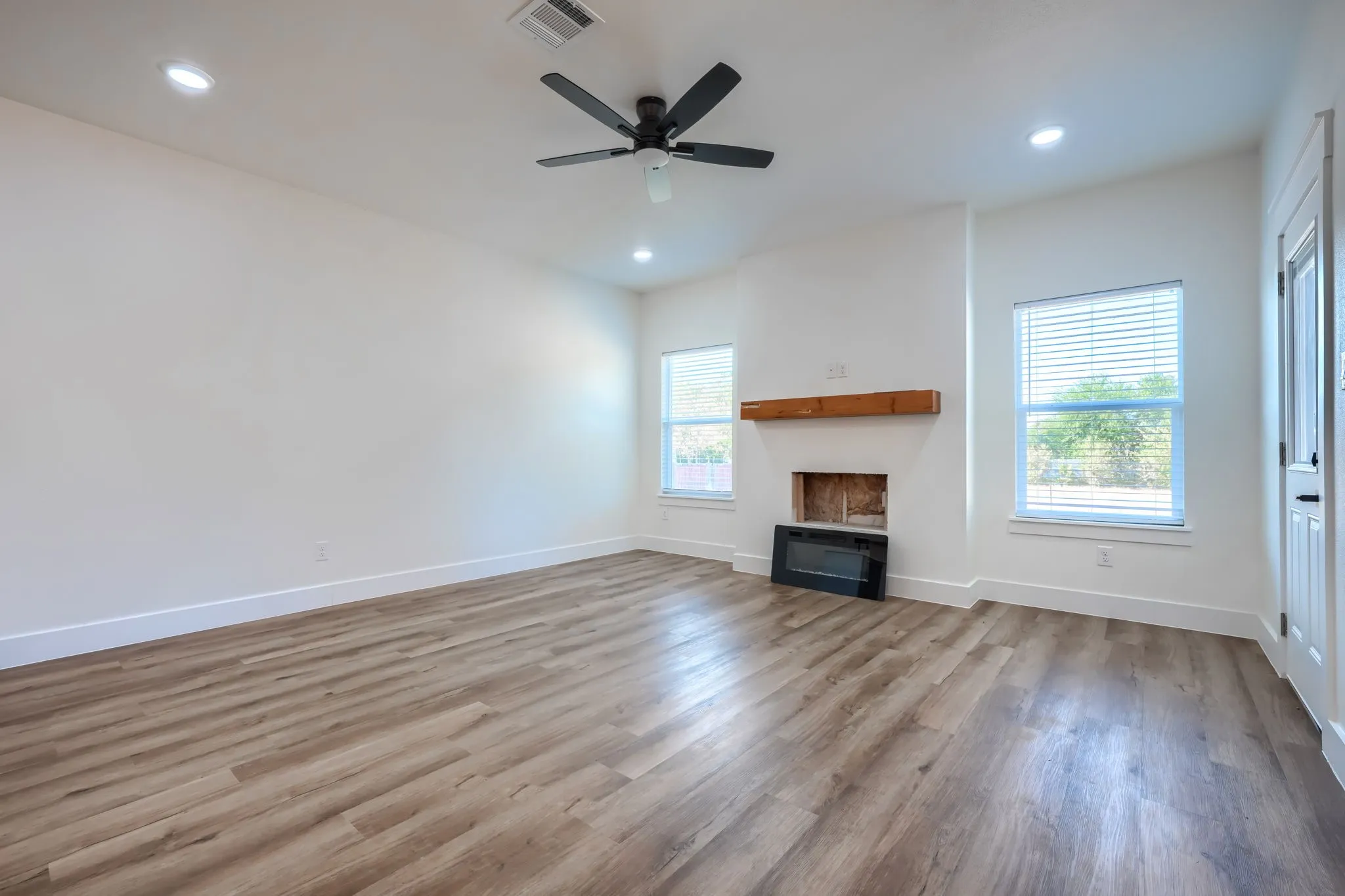 Wood-finish flooring, recessed lighting, ceiling fan, white paneled door, and a fireplace with a wood mantel