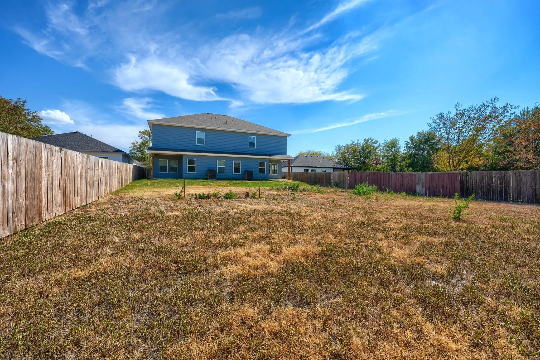 Expansive backyard featuring a privacy fence and a two-story residence with multiple windows