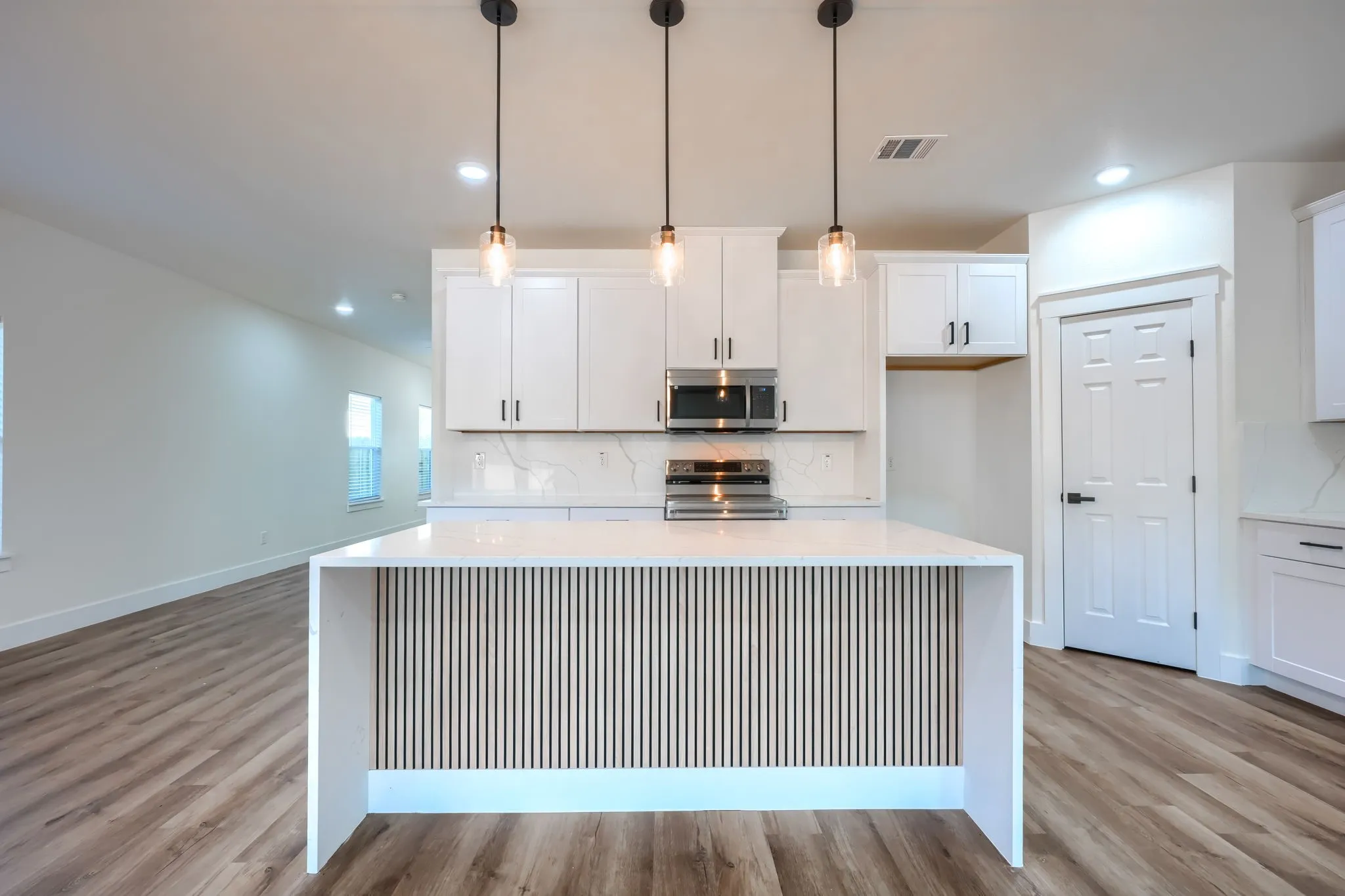 Open-concept kitchen with a waterfall island, white cabinetry, integrated microwave, and wood-finish flooring