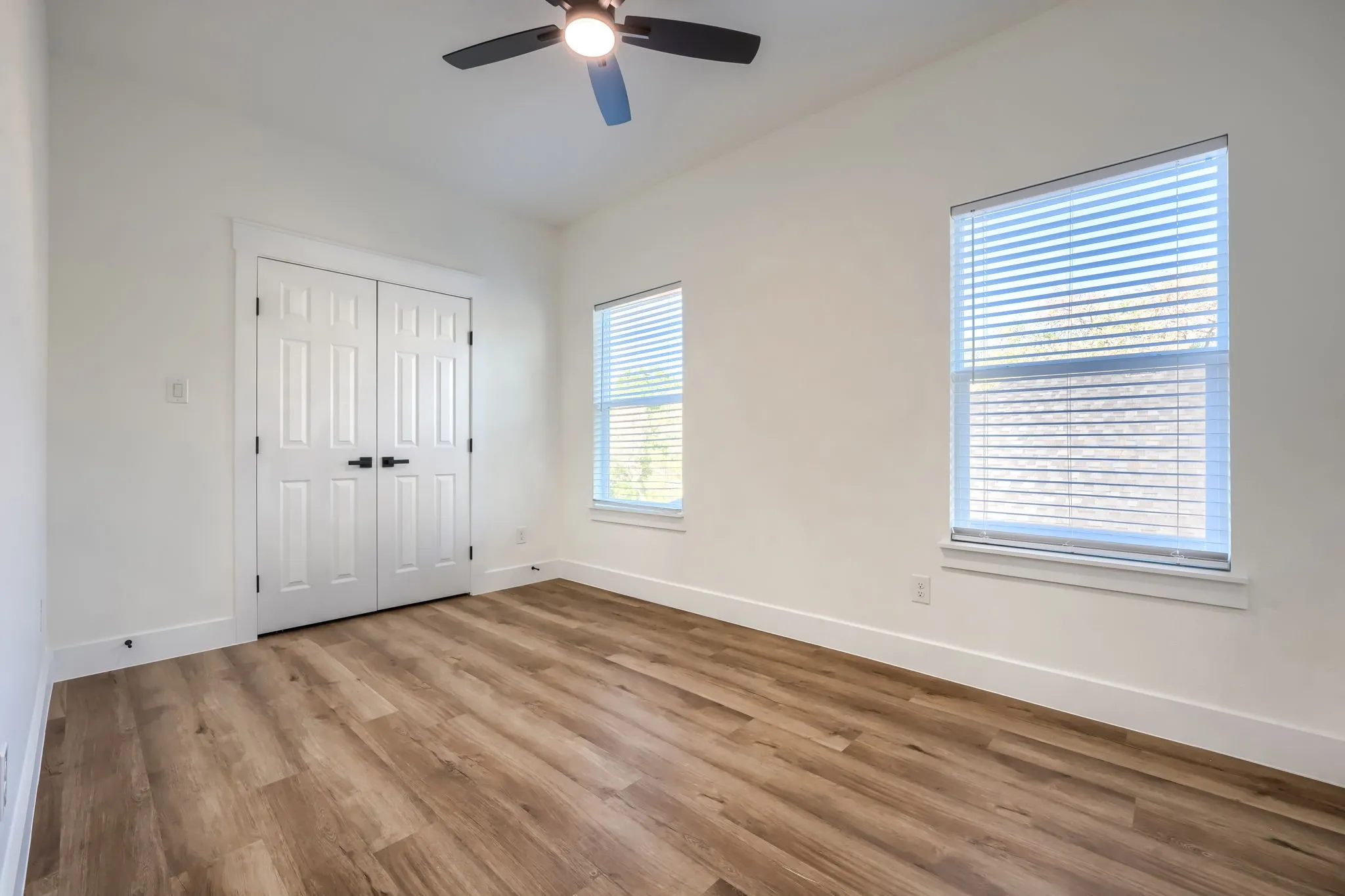 Wood-finish flooring with white trim, a ceiling fan, and multiple windows