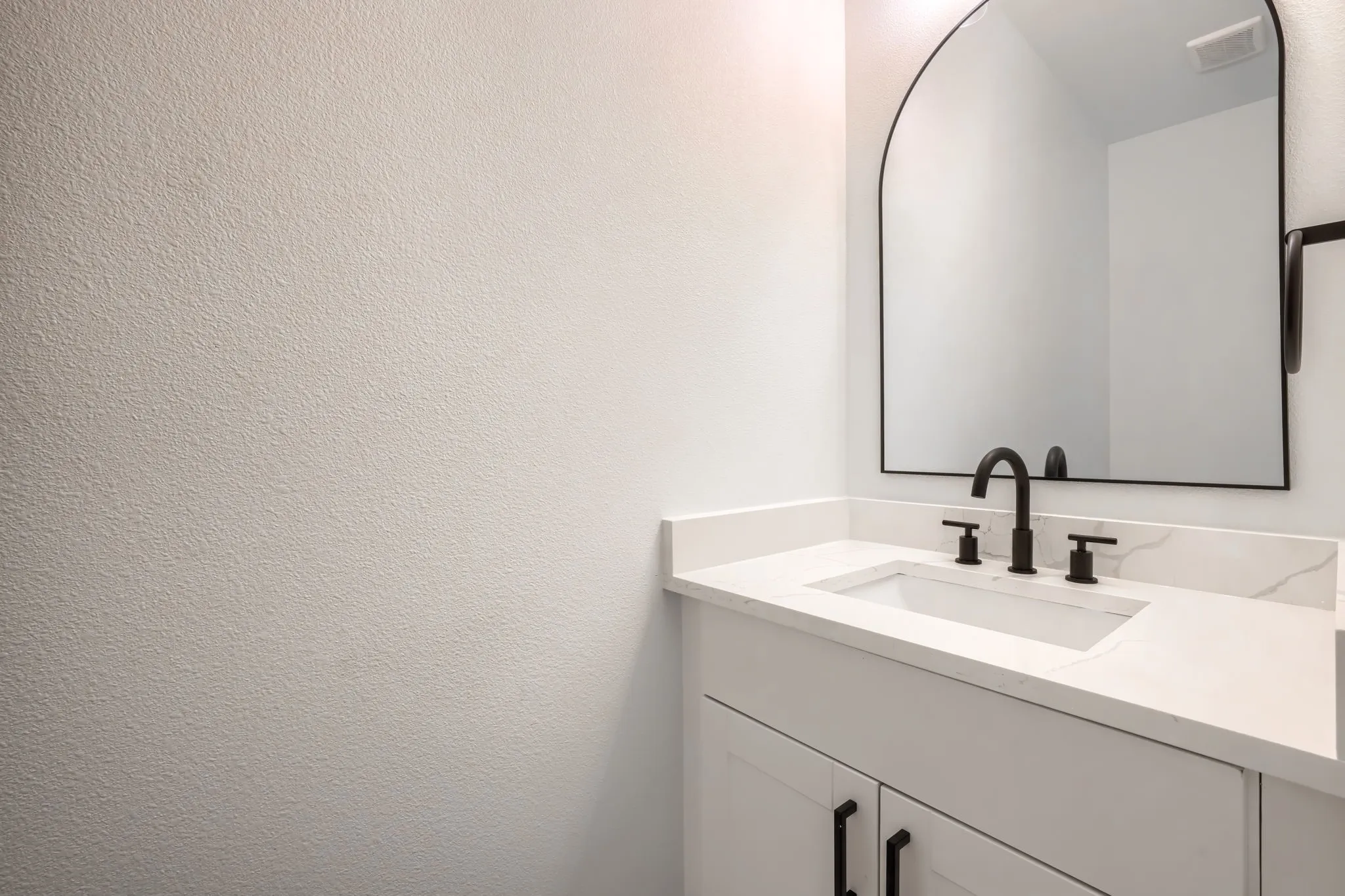 White vanity with a rectangular undermount sink, a white countertop, and a black faucet