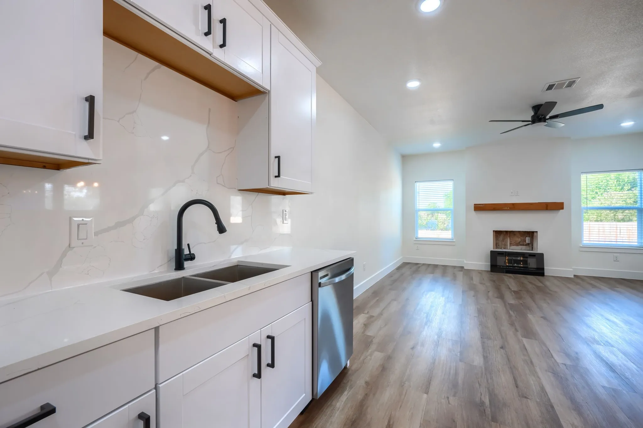 White shaker cabinetry with black hardware, stainless steel double basin sink, stone-look countertop, wood-finish flooring, and recessed lighting