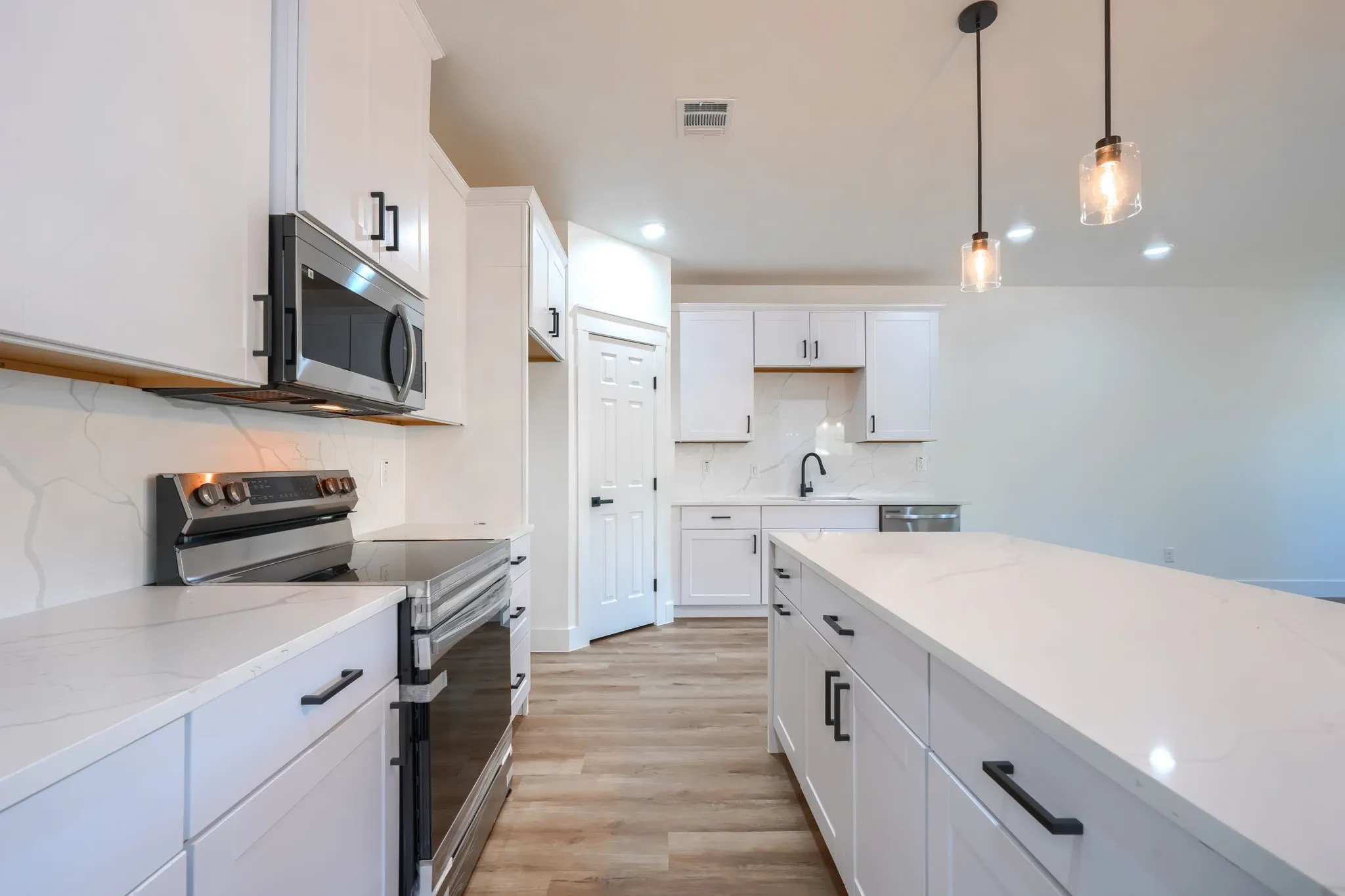 Kitchen featuring white cabinetry, light-toned wood-finish flooring, stainless steel appliances, a center island with a white countertop, and pendant lighting