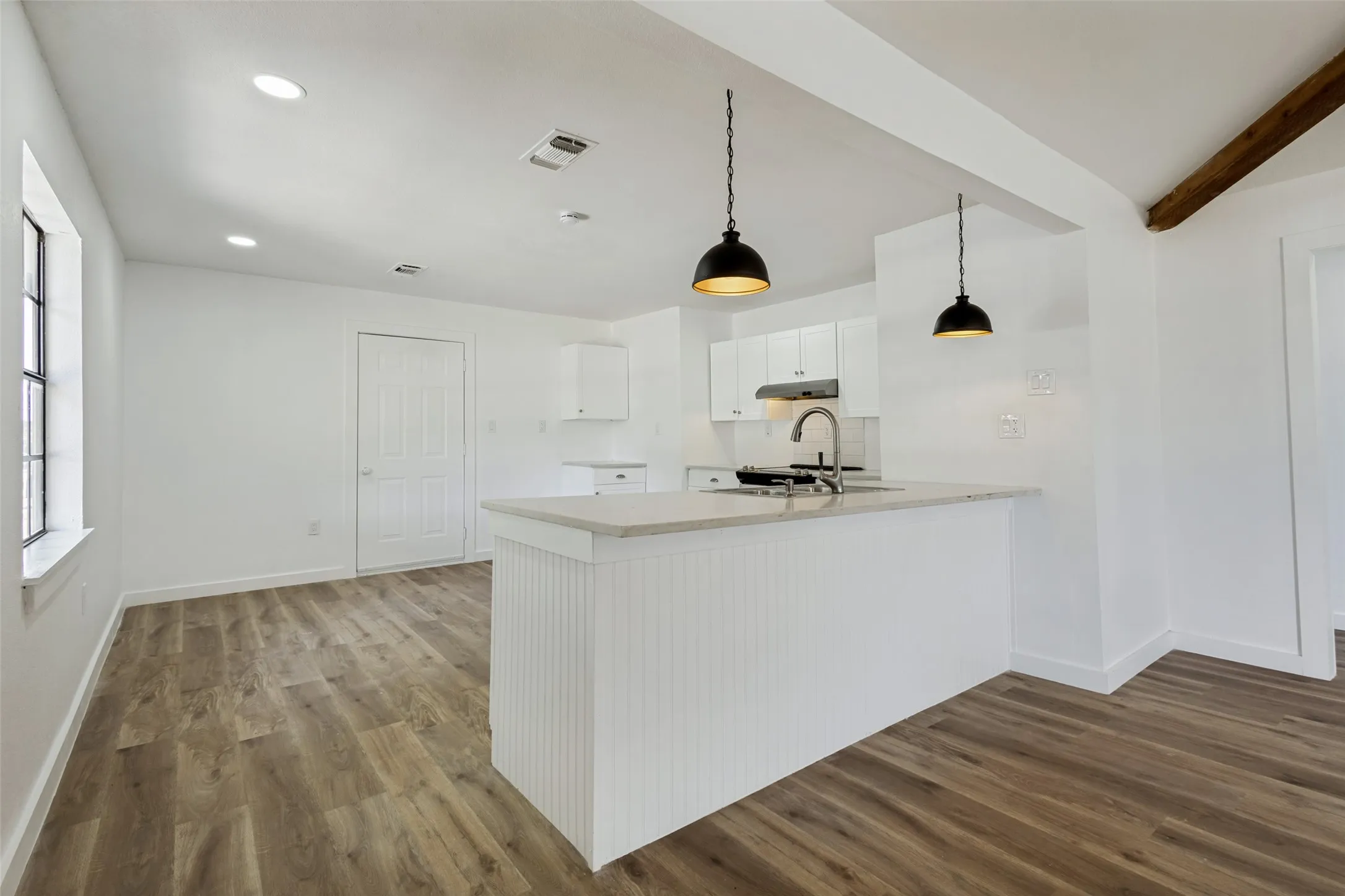 Open-concept kitchen and living area featuring wood-finish flooring, white cabinetry, a light-toned countertop, and two pendant lights above the island
