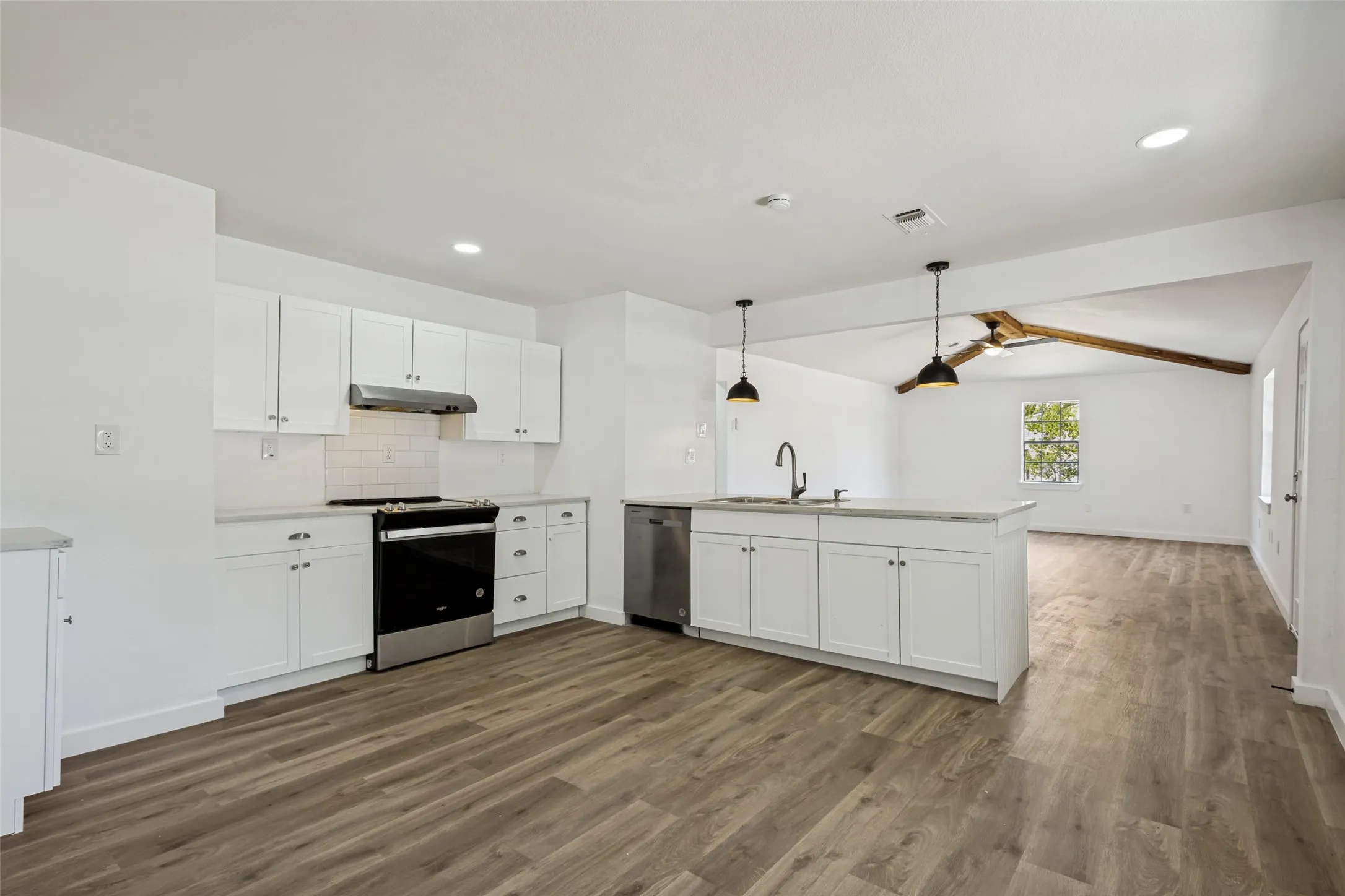 Open-concept kitchen featuring white cabinetry, stainless steel appliances, an island with sink, wood-finish flooring, and recessed lighting