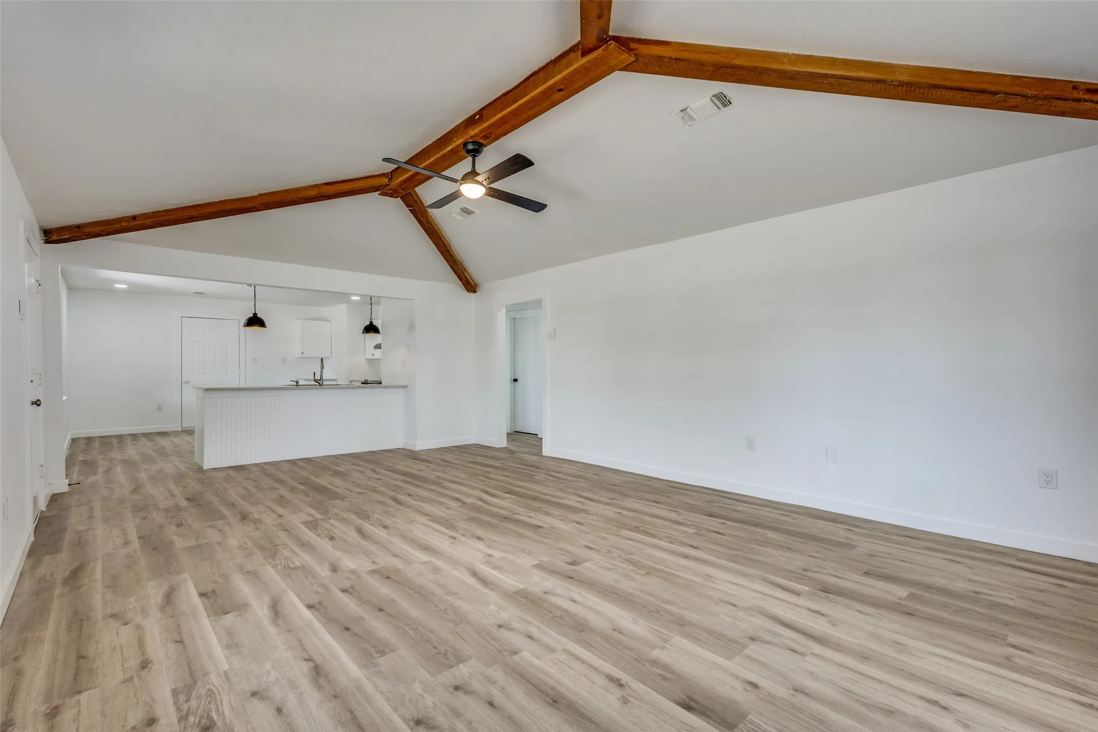 Vaulted ceiling with exposed wood beams, wood-finish flooring, and an open-concept layout