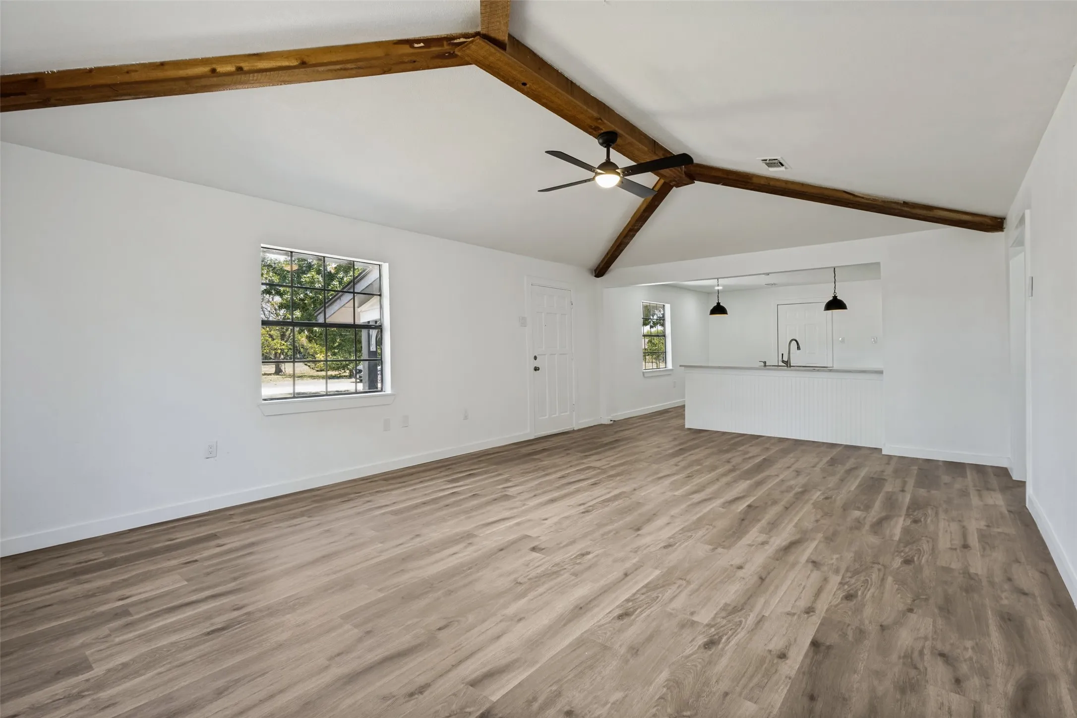 Vaulted ceiling with exposed wood beams, wood-finish flooring, recessed lighting, ceiling fan, and a kitchen pass-through with pendant lighting