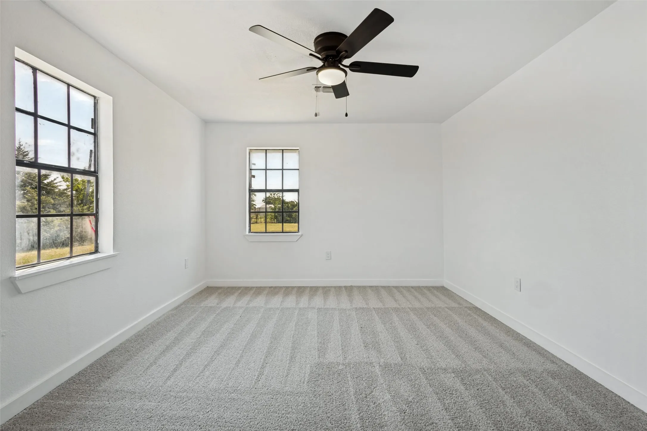 Bright interior space featuring a ceiling fan, two windows with gridded panes, and light-toned carpet