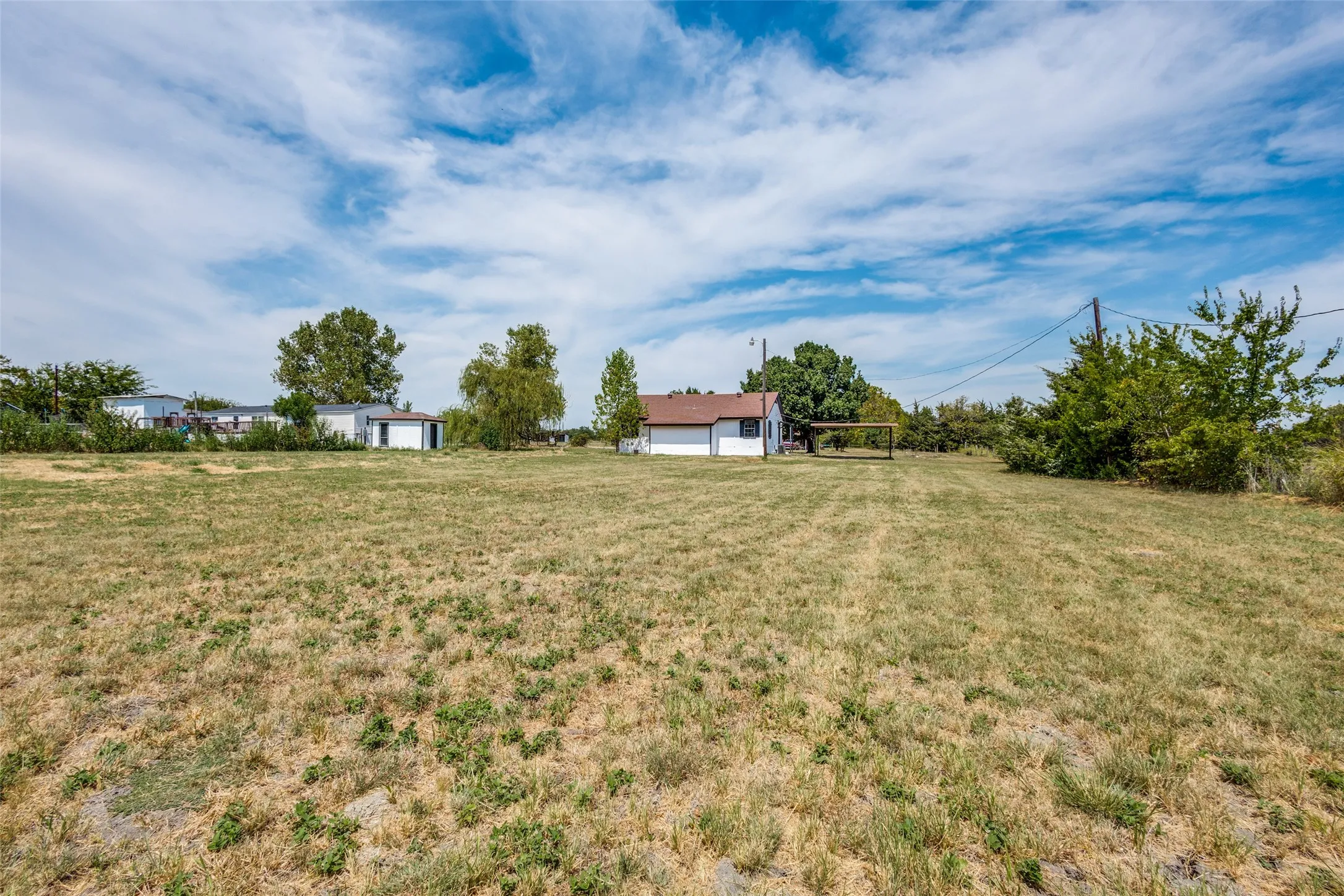 Expansive lot featuring a single-story residence with a brown roof, white exterior siding, and a detached carport structure