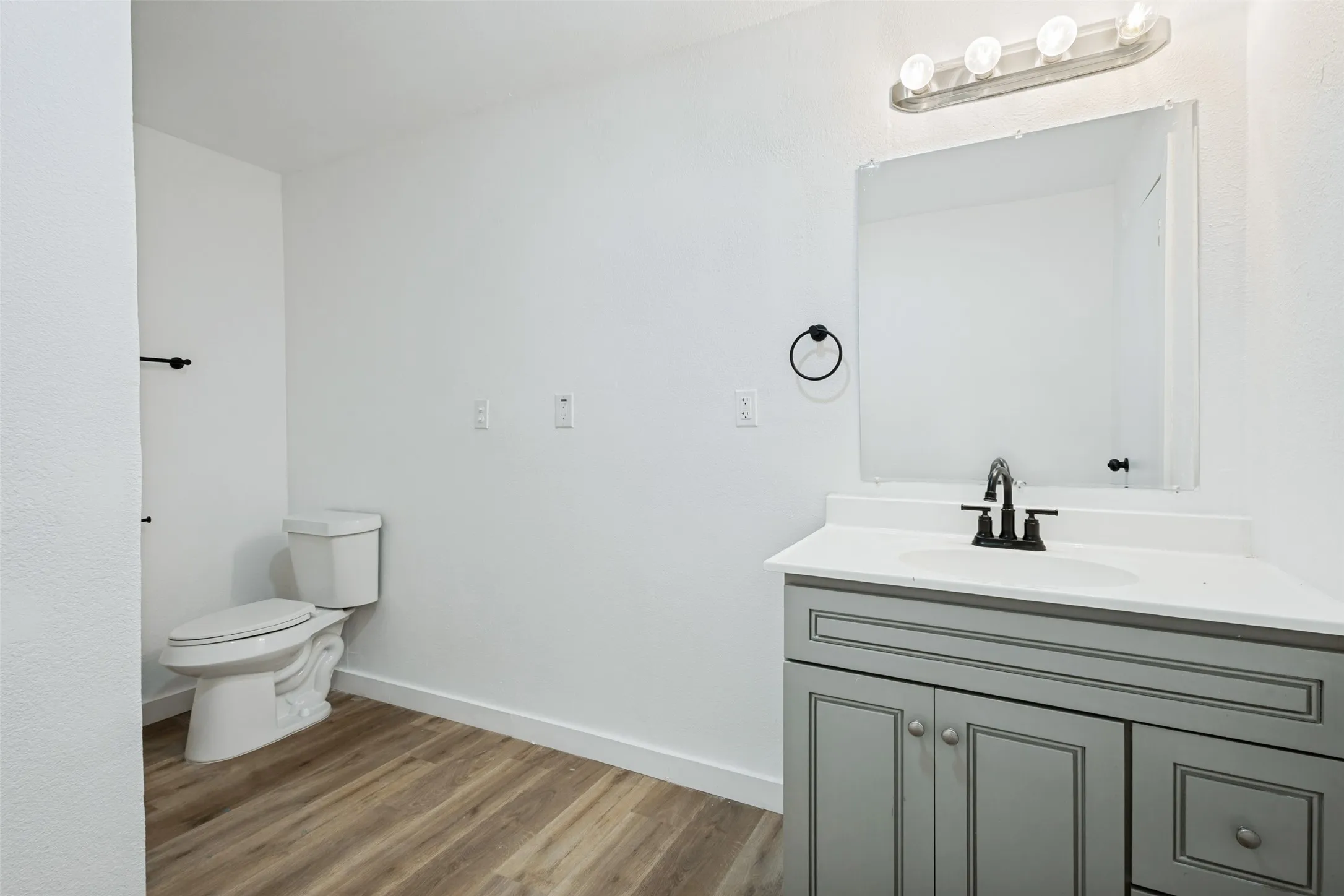 Wood-finish flooring, single vanity with a white countertop, undermount sink, and matte black faucet, wall-mounted mirror, and white toilet