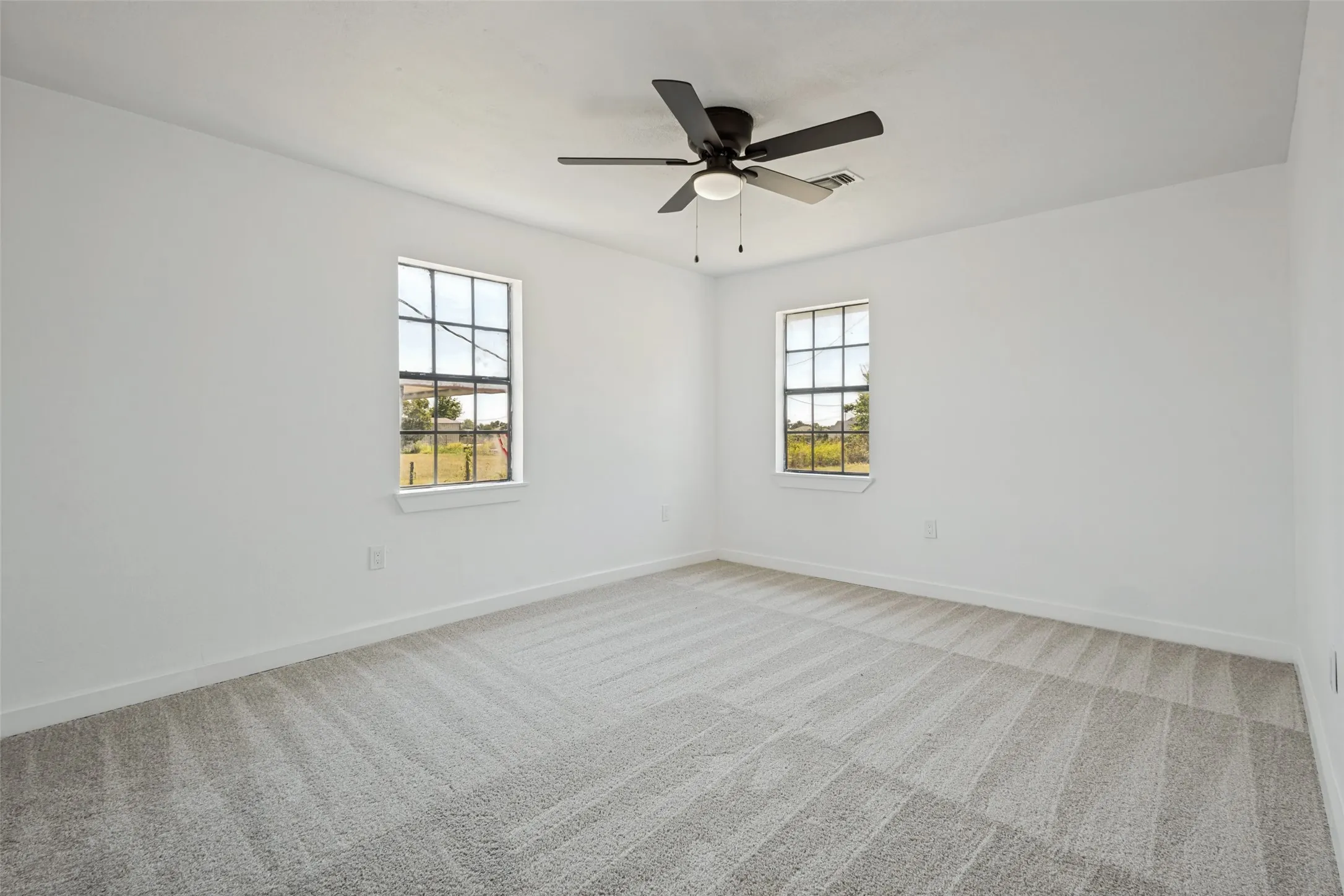 Wall-to-wall carpeting with a striped pattern, two multi-pane windows, and a ceiling fan with integrated lighting