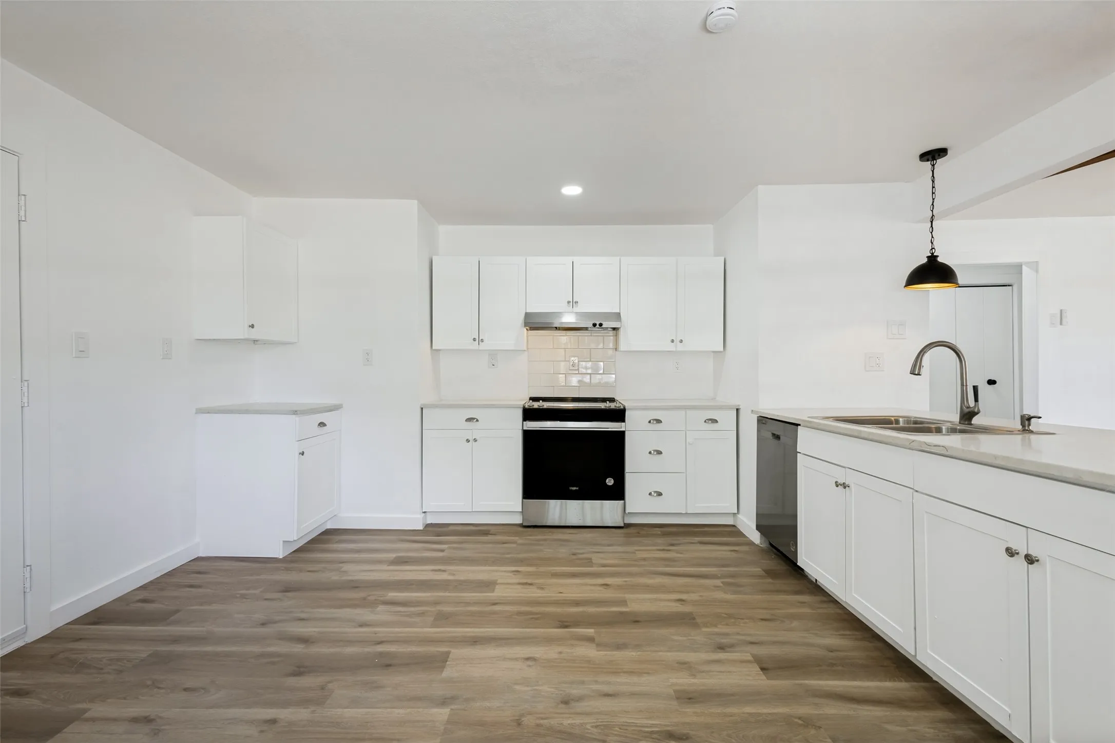 White cabinetry, wood-finish flooring, stainless steel appliances, modern pendant lighting, and light-toned countertops